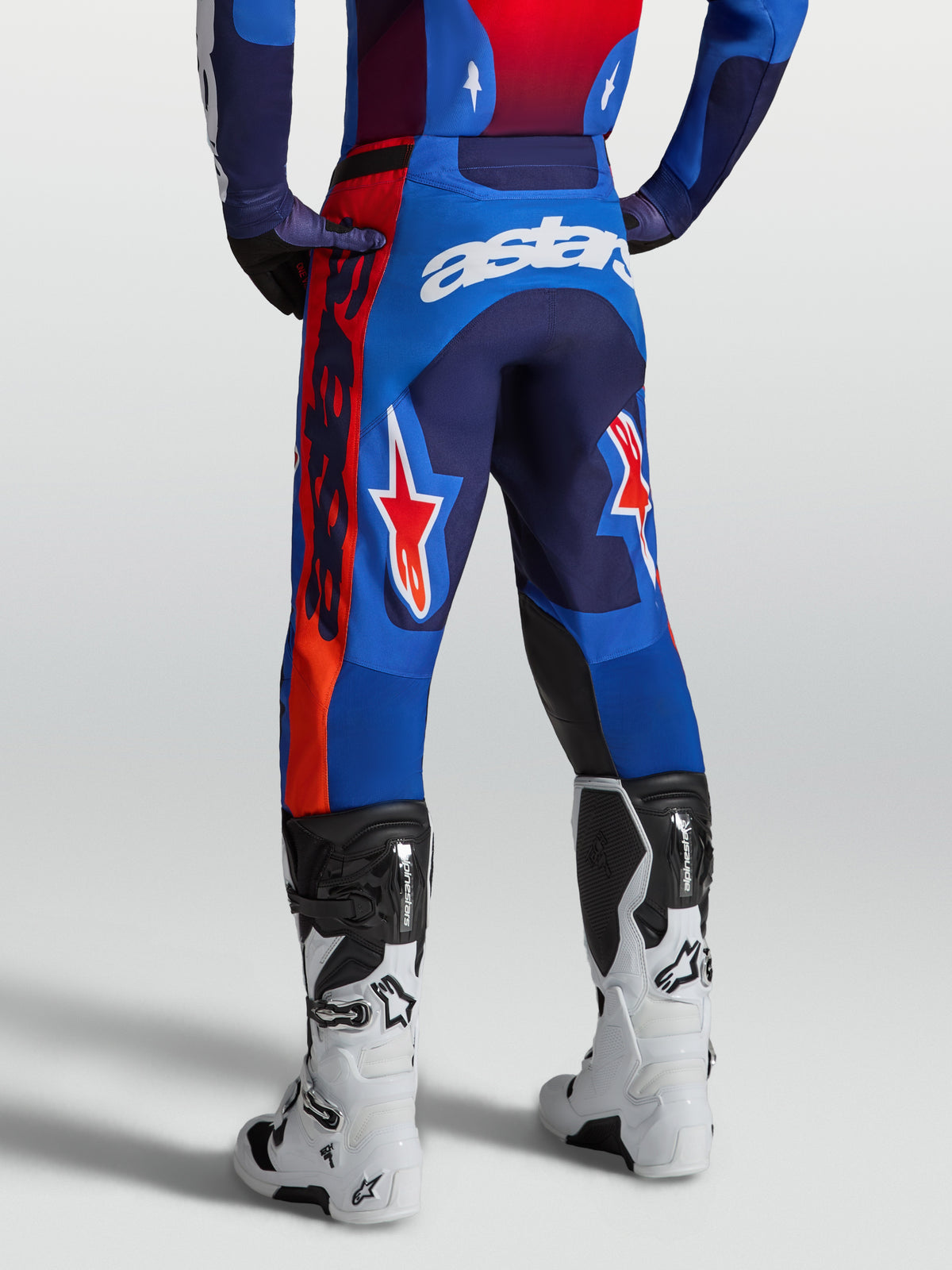 Alpinestars Racer Hunt byxor, blå och röda motocrossbyxor med racingpassform, vy bakifrån på modell med vita stövlar och Astars-logotyper.
