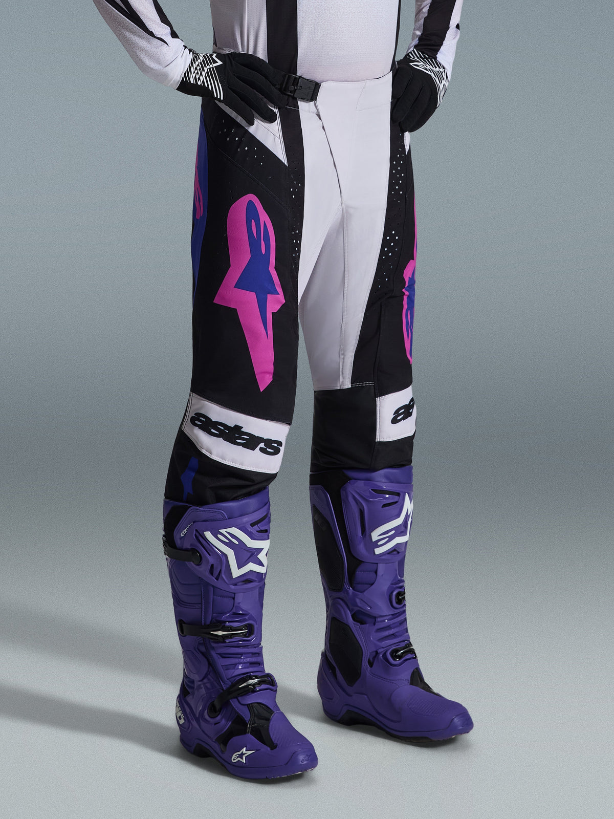 Alpinestars 2026 Techstar Knif-byxor, svarta, ljusgrå och lila, bärs med matchande lila motocross-stövlar, framträdande rosa detaljer och 'astars'-branding, professionell motocrossutrustning