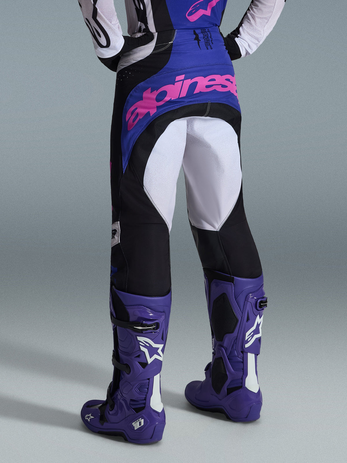 Alpinestars 2026 Techstar Knif byxor, motocrossbyxor, svarta, ljusgrå och lila, vy bakifrån med rosa logotyp på sätet, bärs med matchande tröja och lila motocross-stövlar, professionell outfit för terrängkörning
