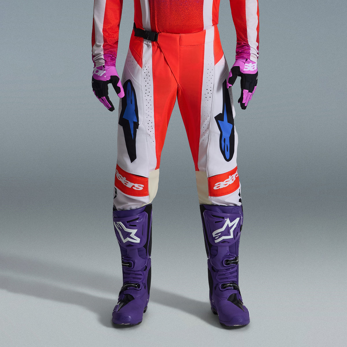 Alpinestars 2026 Techstar Knif Gear Set, underkroppen på en motocrossförare som bär röda och vita byxor med blå detaljer, lila racingstövlar med vita logotyper och matchande svarta och lila handskar, professionellt utrustningsset för terrängkörning