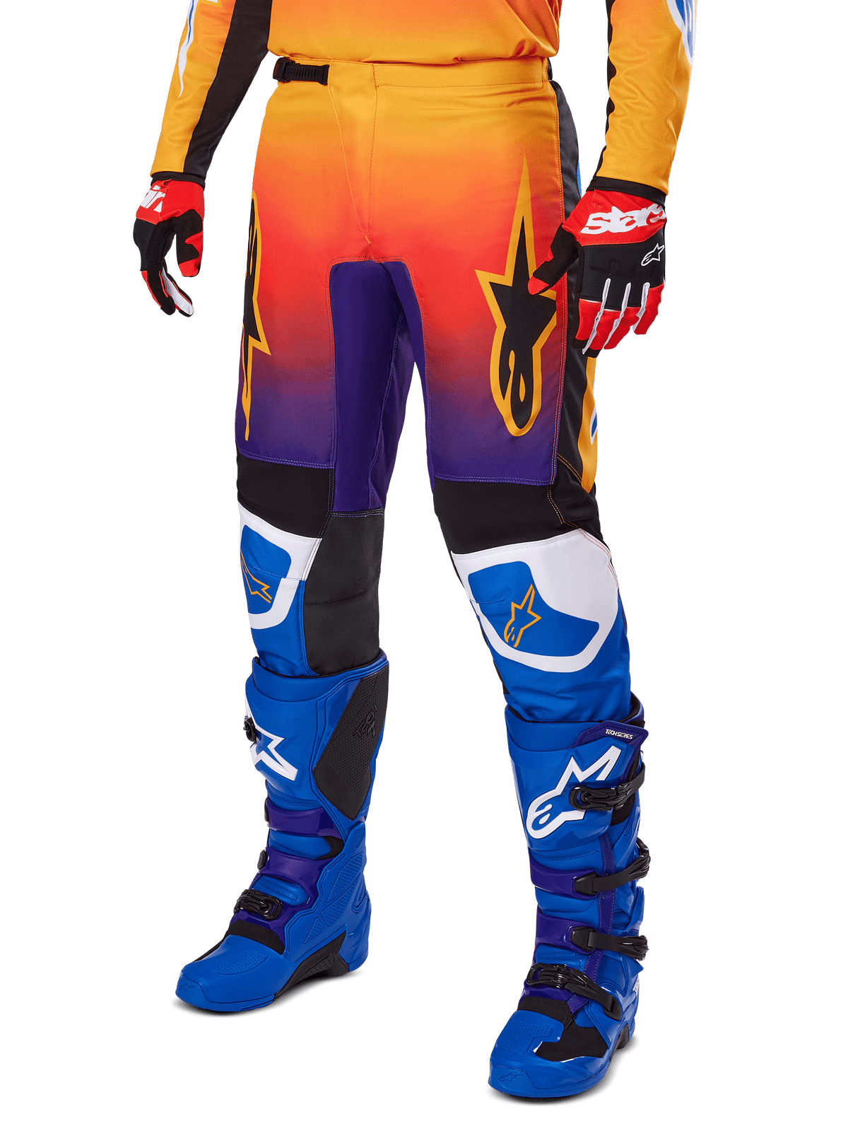 Alpinestars 2025 Fluid Wurx byxor, motocrossbyxor, flerfärgad toning i orange, rött och lila med svarta och blå paneler, bärs med blå stövlar och röda handskar, stjärnlogotyper och vita detaljer vid knäna, hållbar prestandautrustning för terrängkörning