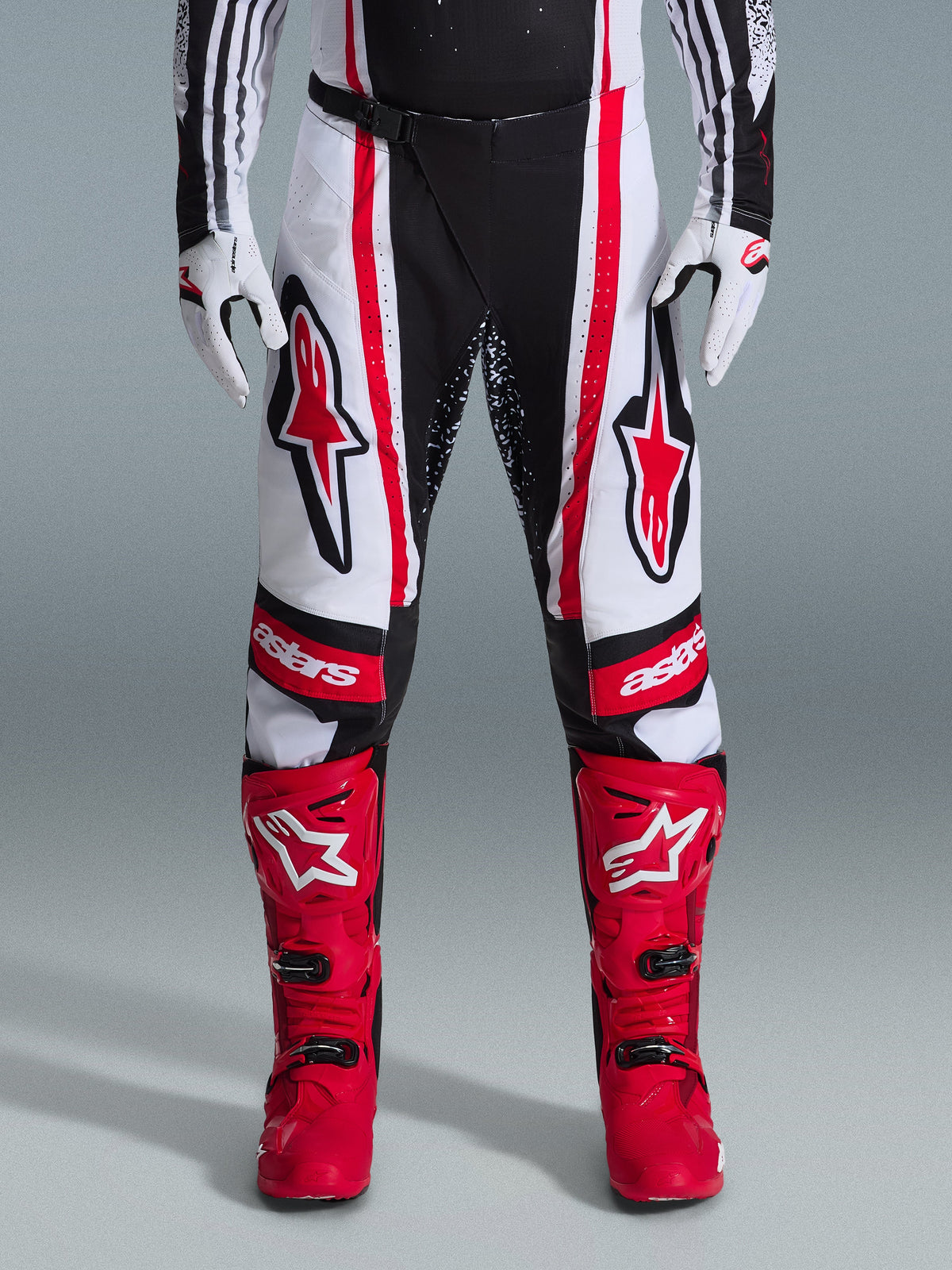 Alpinestars 2026 Techstar Nomur-byxor, motocrossbyxor, svarta, vita och röda, bärs med matchande röda stövlar och vita handskar, framträdande röda logotyper på låren och 'astars'-märkning på knäna, flerpanelad racingdesign för off-road-prestanda