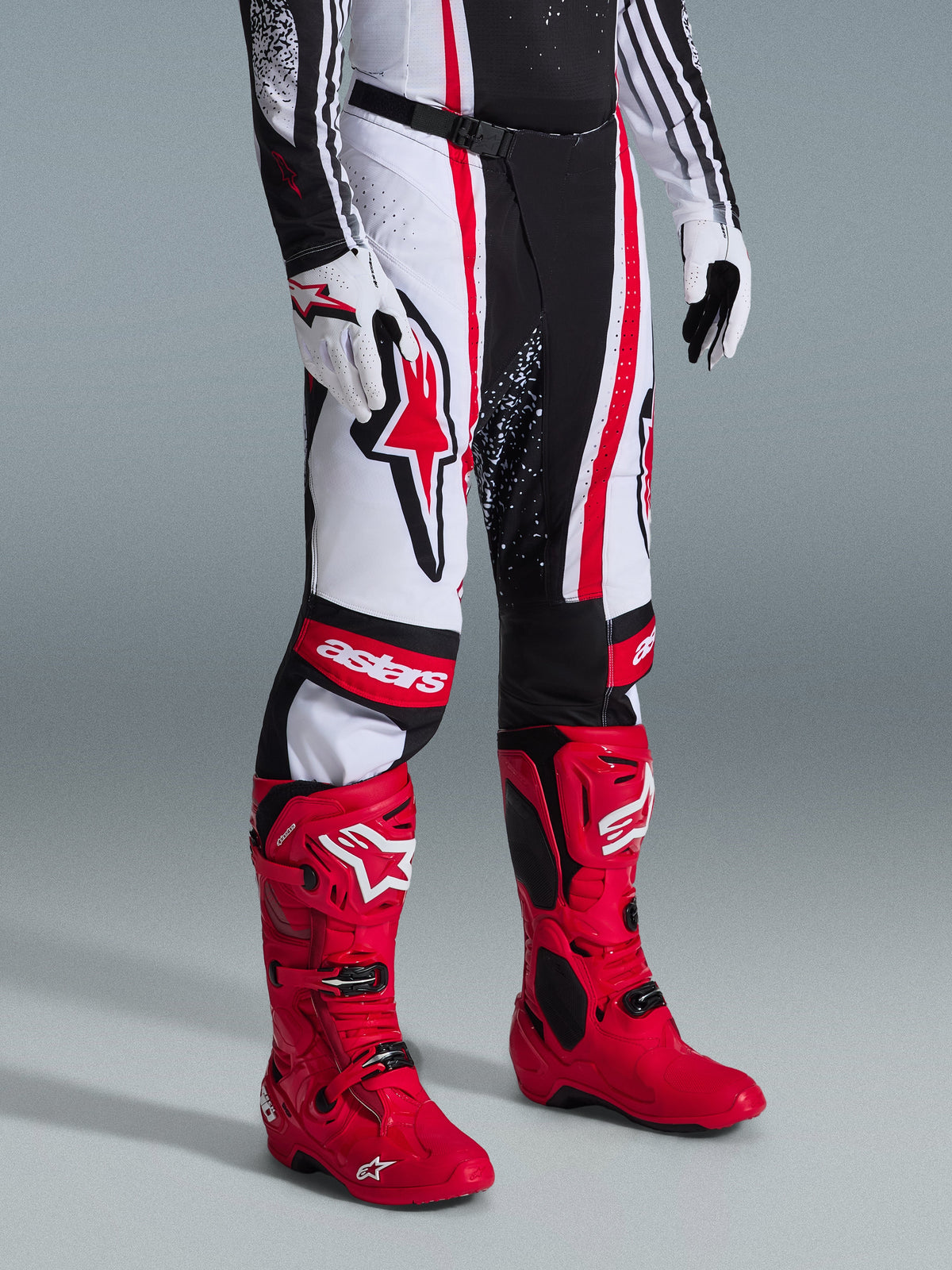 Alpinestars 2026 Techstar Nomur byxor, motocrossbyxor, svart, vit och röd, bärs med kraftigt röda racingstövlar och vita handskar, framträdande vertikala ränder, en stor röd stjärnlogotyp på låret och förstärkta knäpaneler för terrängkörning.
