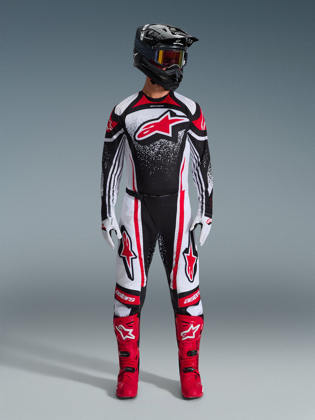 Alpinestars 2026 Techstar Nomur utrustningsset, motocrossförare stående i full racingutrustning, svart, vit och röd design med vitt stänkmönster, tröja med röd Astars-logotyp, matchande vita och röda byxor, klarröda stövlar och svart hjälm med goggles, koordinerat högpresterande motocross-kit