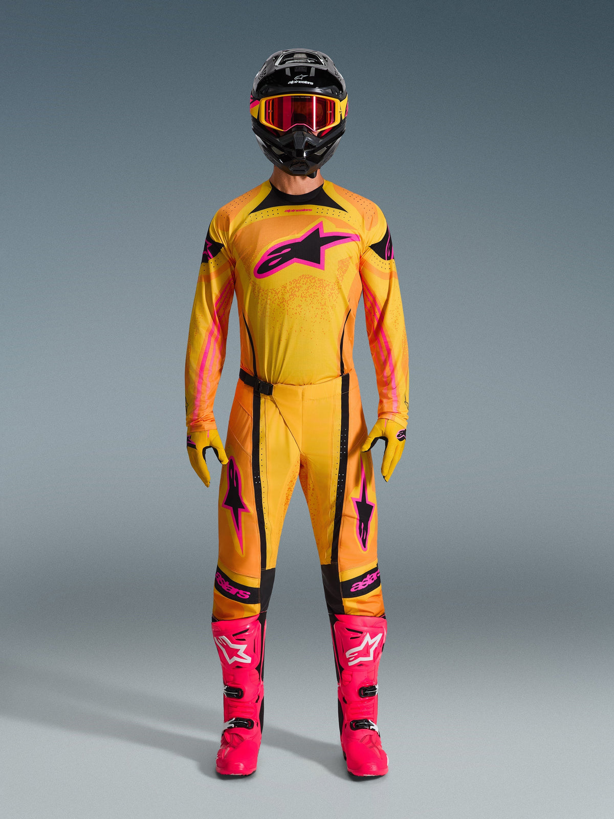 Motocross rider wearing full Alpinestars 2026 Techstar Nomur gear set, Orange Yellow and Pink jersey and pants, matching yellow and pink gloves, vibrant pink racing boots, and black helmet with pink goggles, coordinated high-performance motocross outfit.