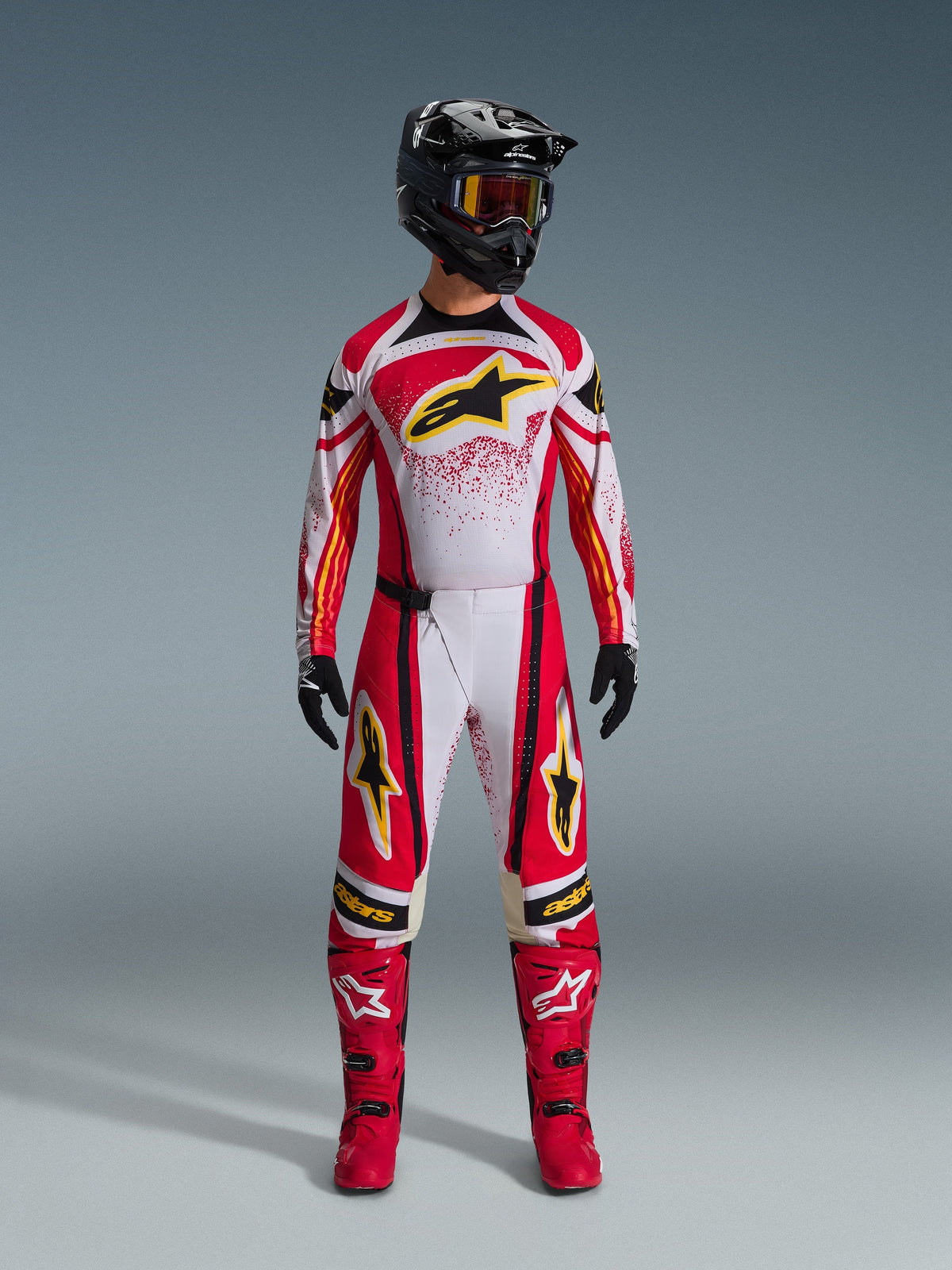 Motocross rider wearing Alpinestars 2026 Techstar Nomur Pants, Red White and Black off-road racing gear, matching jersey with yellow star logo, black helmet with goggles, red boots, and black gloves, coordinated outfit for motocross
