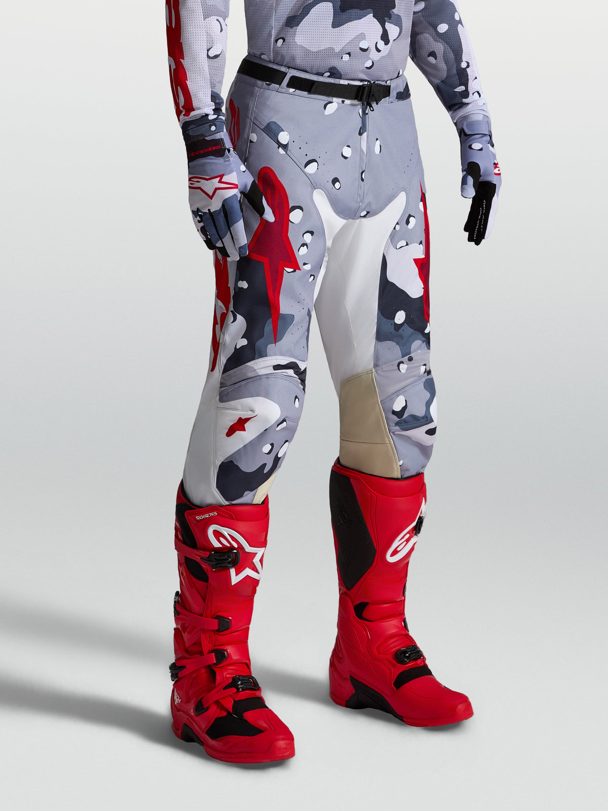 Alpinestars Racer Air Lone byxor, motocrossbyxor i grå camo-design med röda detaljer, perforerat material för optimalt luftflöde vid terrängkörning, visas på modell.