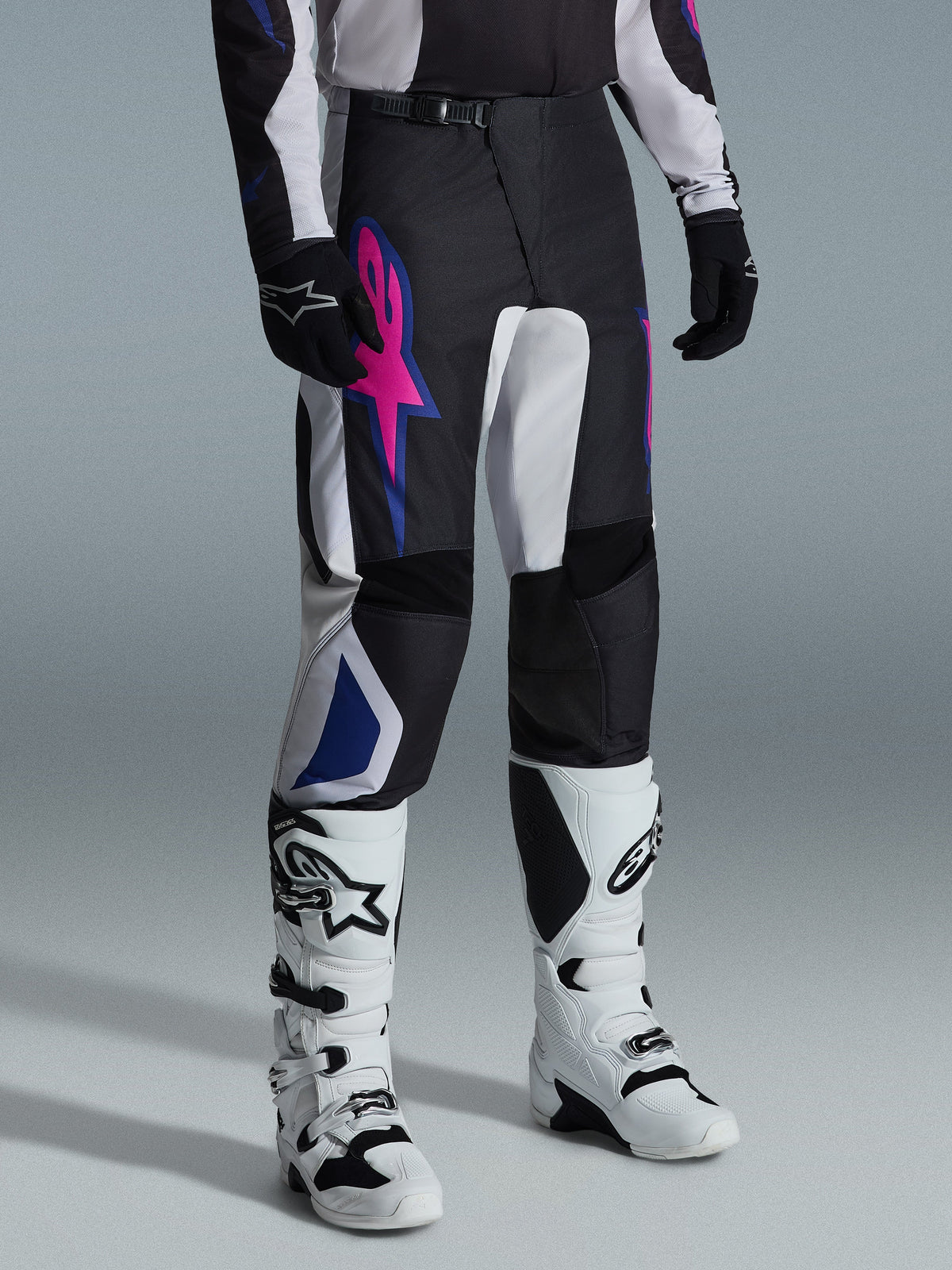 Alpinestars 2026 Fluid Grid Pants, Motocross Pants, Black Light Gray and Purple, featuring a bold pink star logo and blue geometric accents, worn with white motocross boots and black gloves, ergonomic off-road riding gear