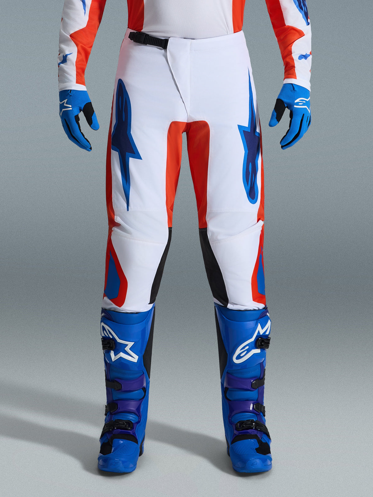 Alpinestars 2026 Fluid Grid byxor, motocrossbyxor, orange och UCLA-blå, bärs med matchande blå stövlar och handskar, vitt chassi med framträdande blå logotyper och orangea detaljer, ergonomisk design för offroad-prestanda