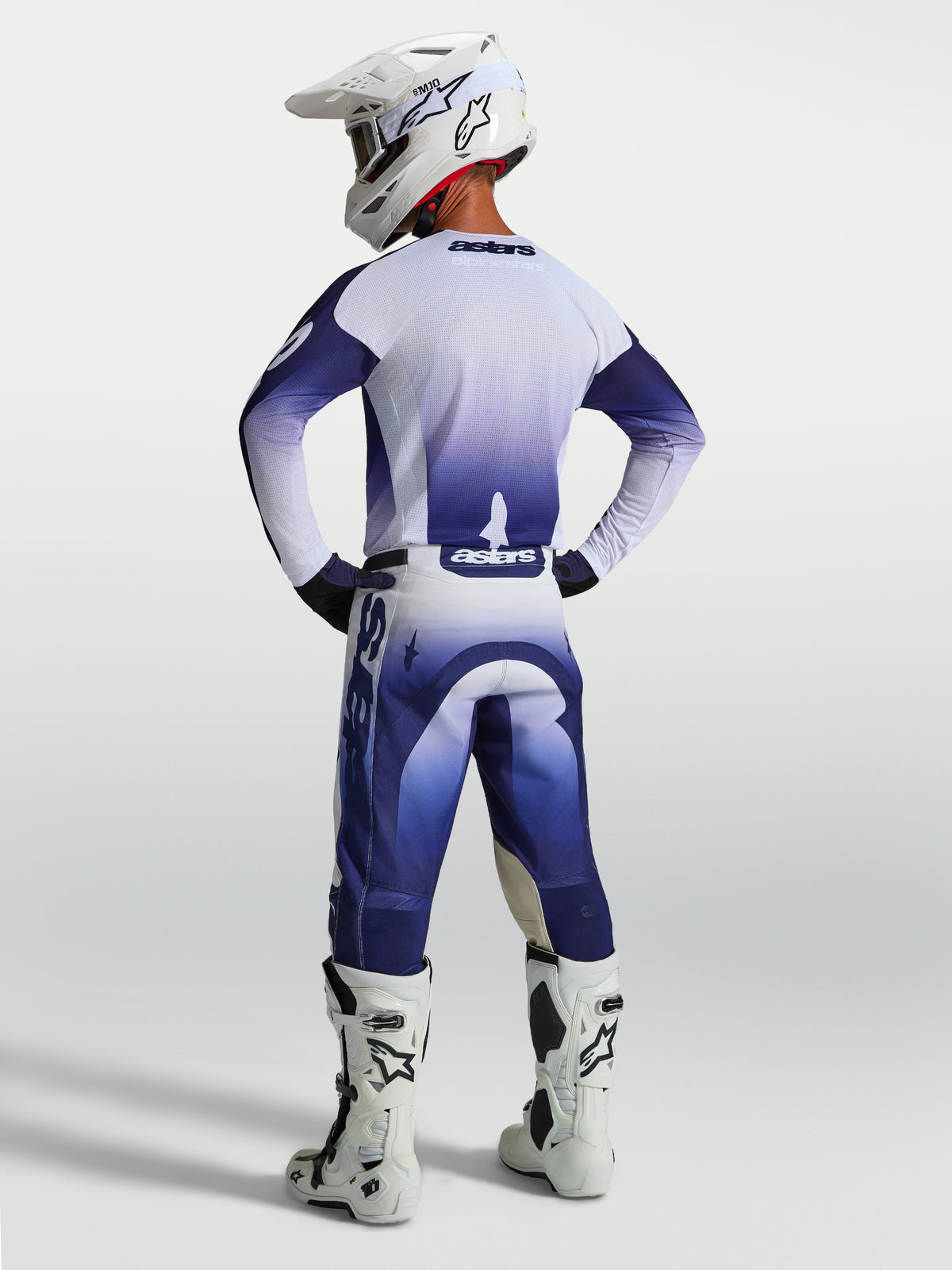 Alpinestars Racer Air Amber byxor, blå och vita motocrossbyxor för herr, högventilerad perforerad konstruktion, visas bakifrån på en förare med vita stövlar och hjälm.