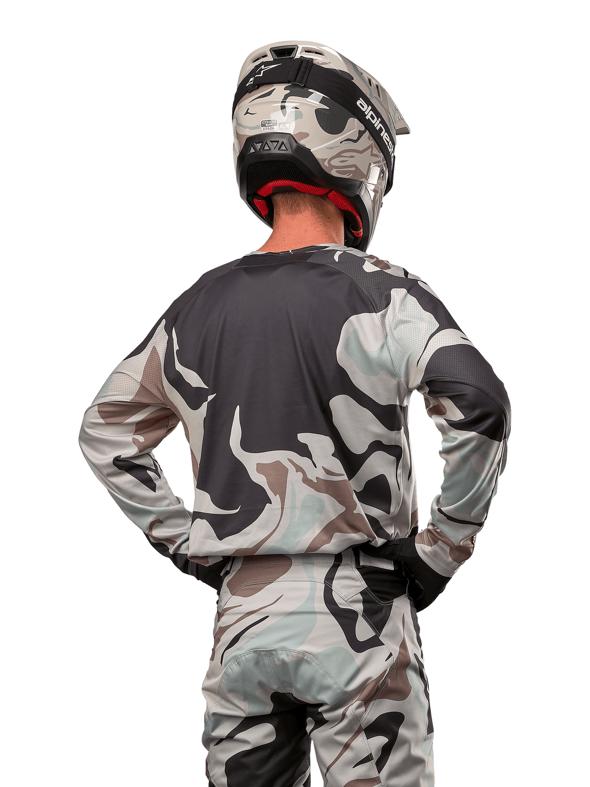 Motocrossförare sedd bakifrån, Alpinestars 2024 Racer Tactical Jersey i Iron Camo Dust Gray, matchande kamouflagebyxor och hjälm, händerna på höfterna, koordinerad racingutrustning för terrängkörning