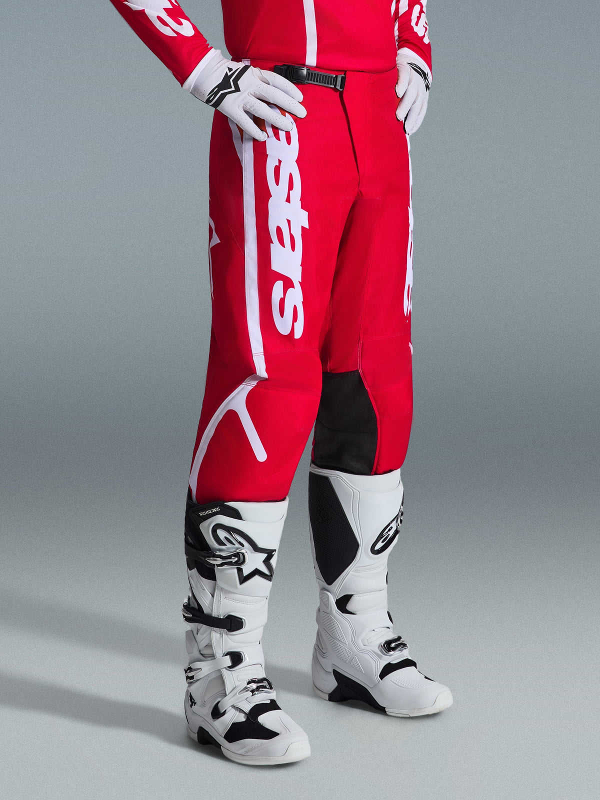 Alpinestars 2026 Fluid Apex byxor, motocrossbyxor, röda och vita, bärs med vita och svarta motocross-stövlar och handskar, med framträdande vit logotyp och svarta paneler på insidan av knäna, designade för offroad-prestanda