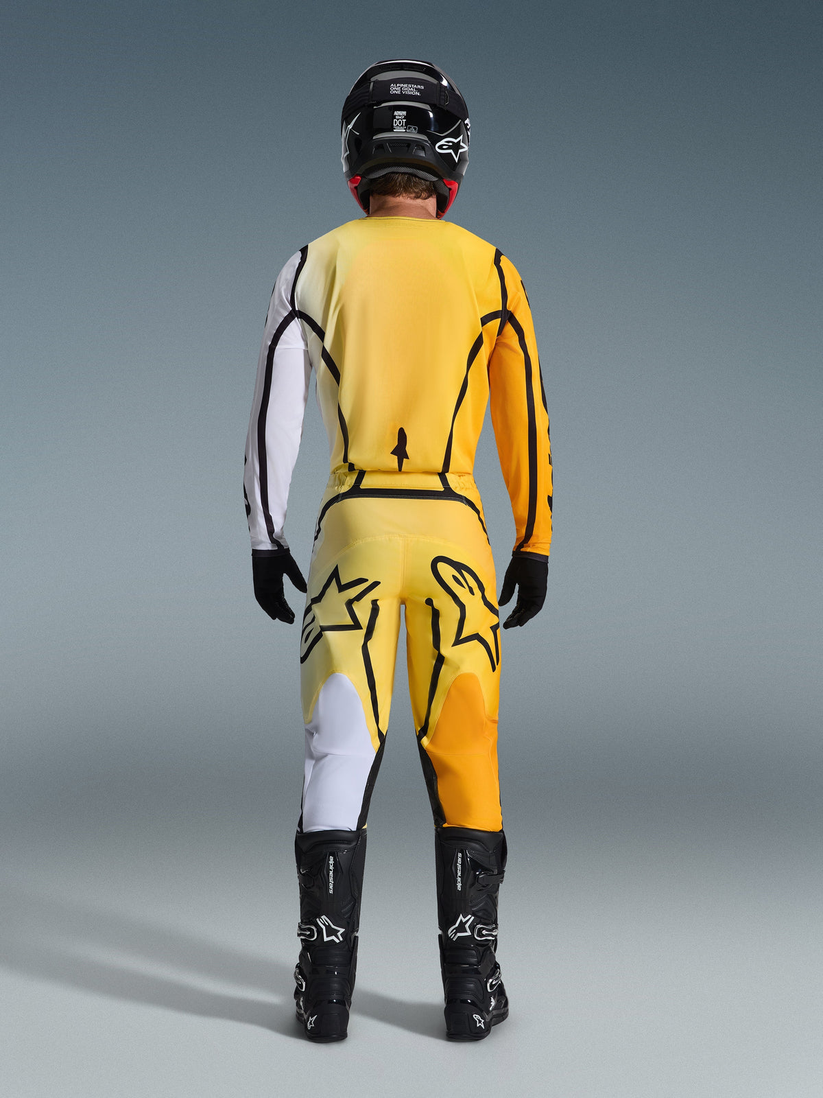 Alpinestars 2026 Fluid Apex Pants, Motocross Pants, Yellow and Black, rear view of a rider in full motocross gear, matching jersey with white and orange gradients, black helmet, black boots, and black gloves, coordinated off-road outfit.
