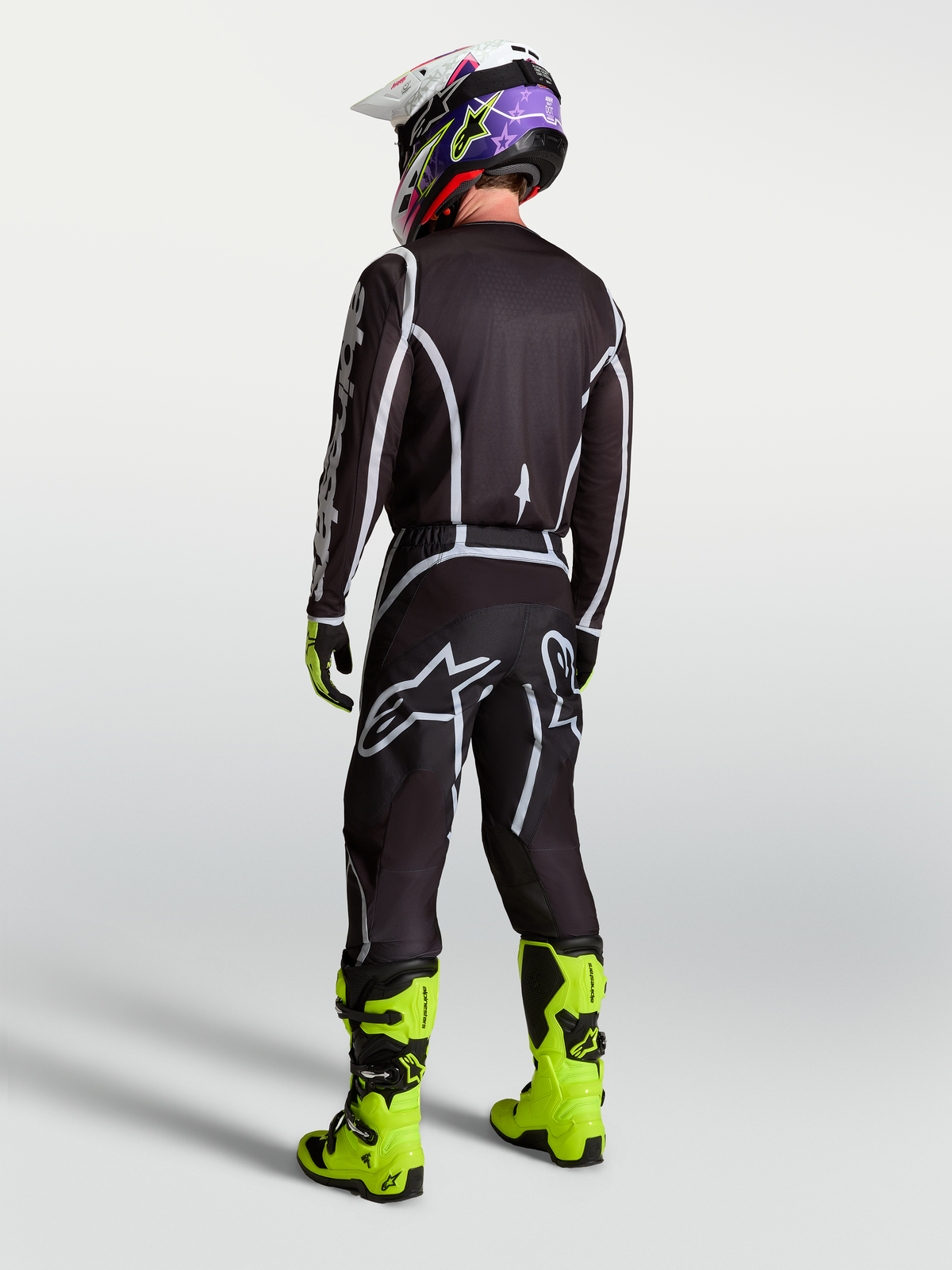 Alpinestars Fluid Apex V2 byxor, motocrossbyxor för herr, svarta och silver, vy bakifrån med tröja och neongula stövlar.
