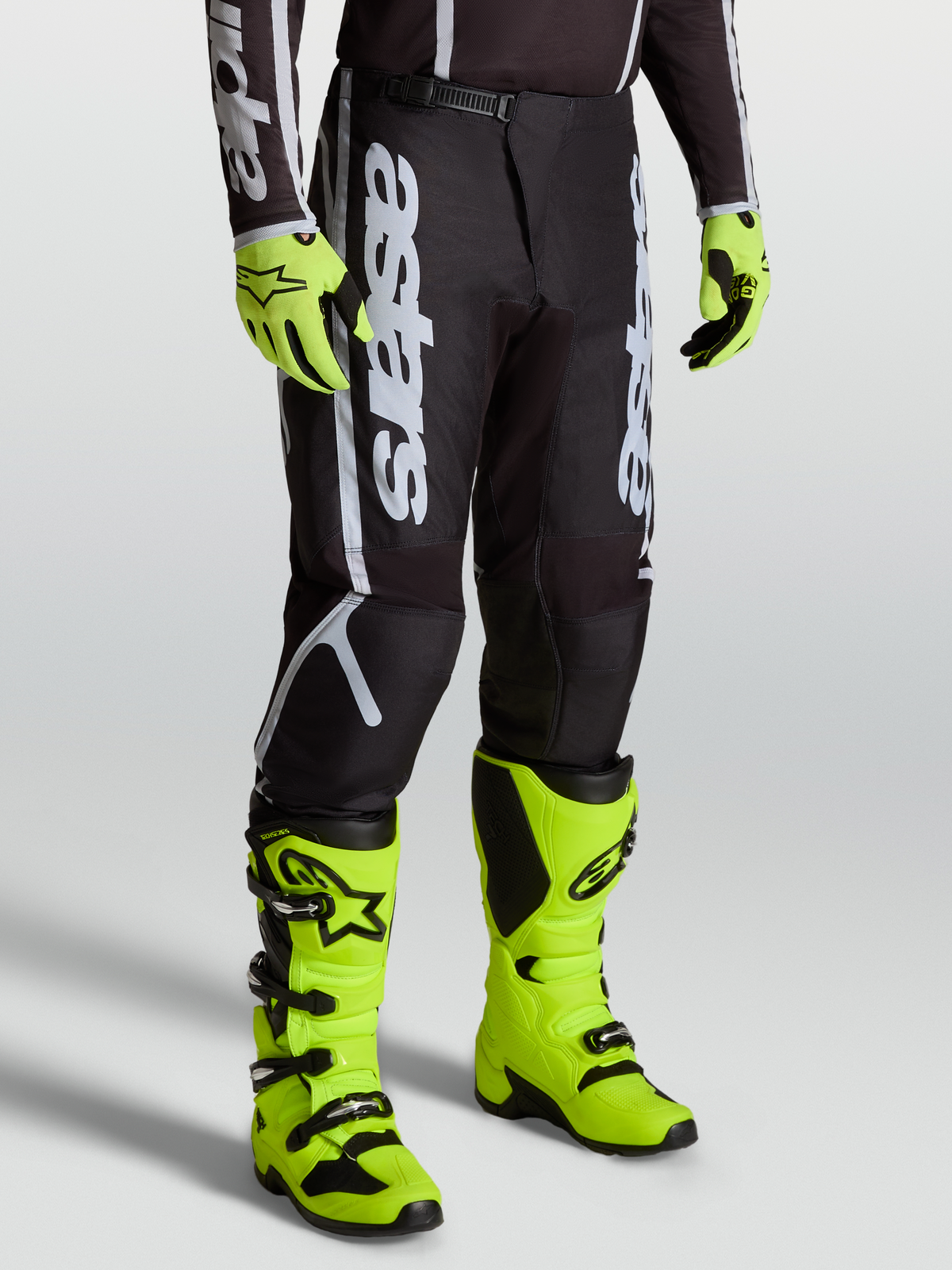 Alpinestars Fluid Apex V2 byxor, svarta och silver motocrossbyxor för herr, 600D polytyg, visas på modell med neongula stövlar