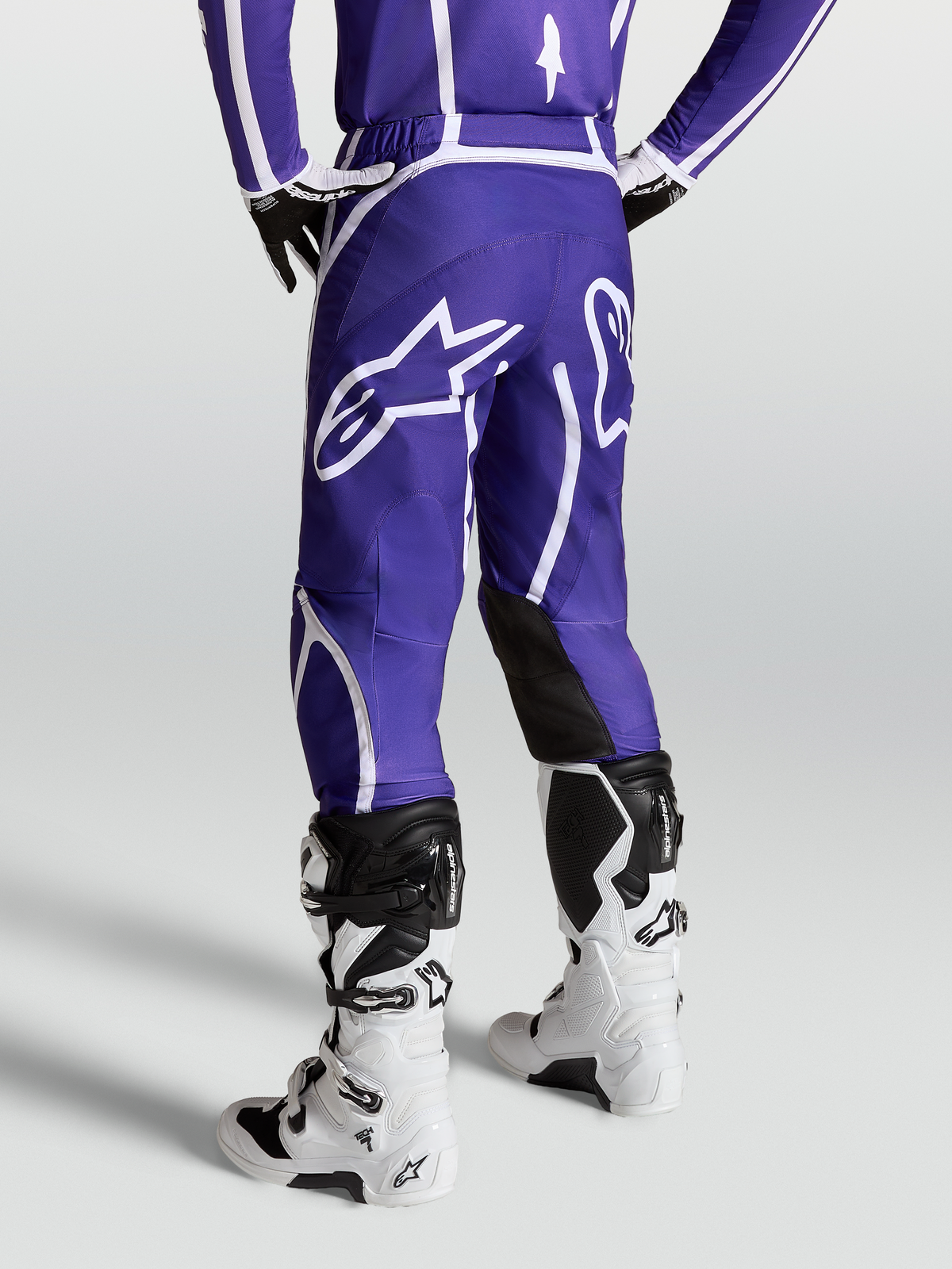Alpinestars Fluid Apex V2 byxor, mörkblå och vita motocrossbyxor för herr, sedda bakifrån på modell med vita stövlar, stor stjärnlogotyp och ergonomisk 3D-skärning.