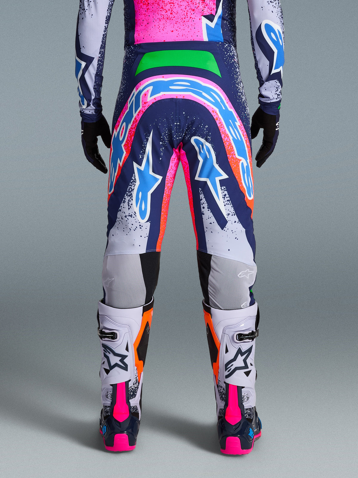 Alpinestars Limited Edition Supertech Records-byxor, motocrossbyxor, flerfärgade med livfull grafik i rosa, blått, orange och vitt, bakifrån som visar en stor logotyp över sätet, bärs med matchande tröja och vita stövlar, atletisk passform på proffsnivå för terrängkörning.