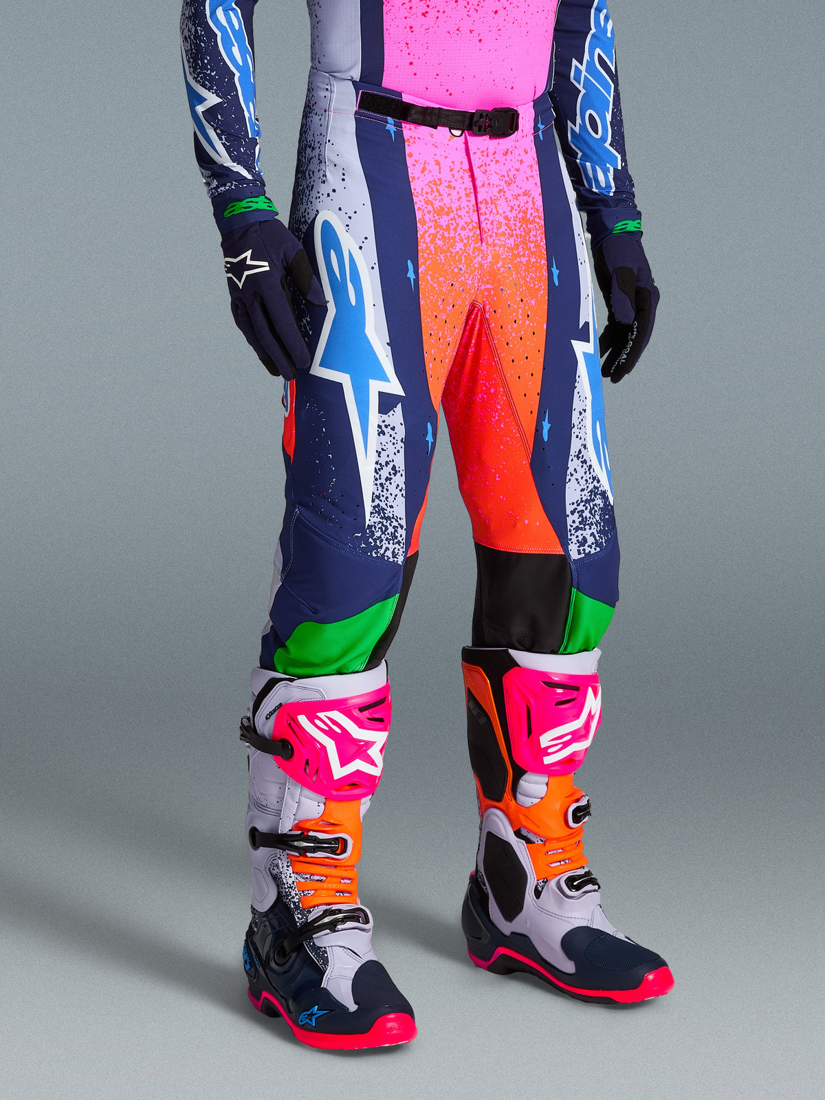 Alpinestars Limited Edition Supertech Records-byxor, livfulla flerfärgade motocrossbyxor med stänkmönstrad grafik i rosa och orange, marinblå och vita paneler, med en stor vit och cyanblå Astars-logotyp, bärs med matchande prestandastövlar och handskar.