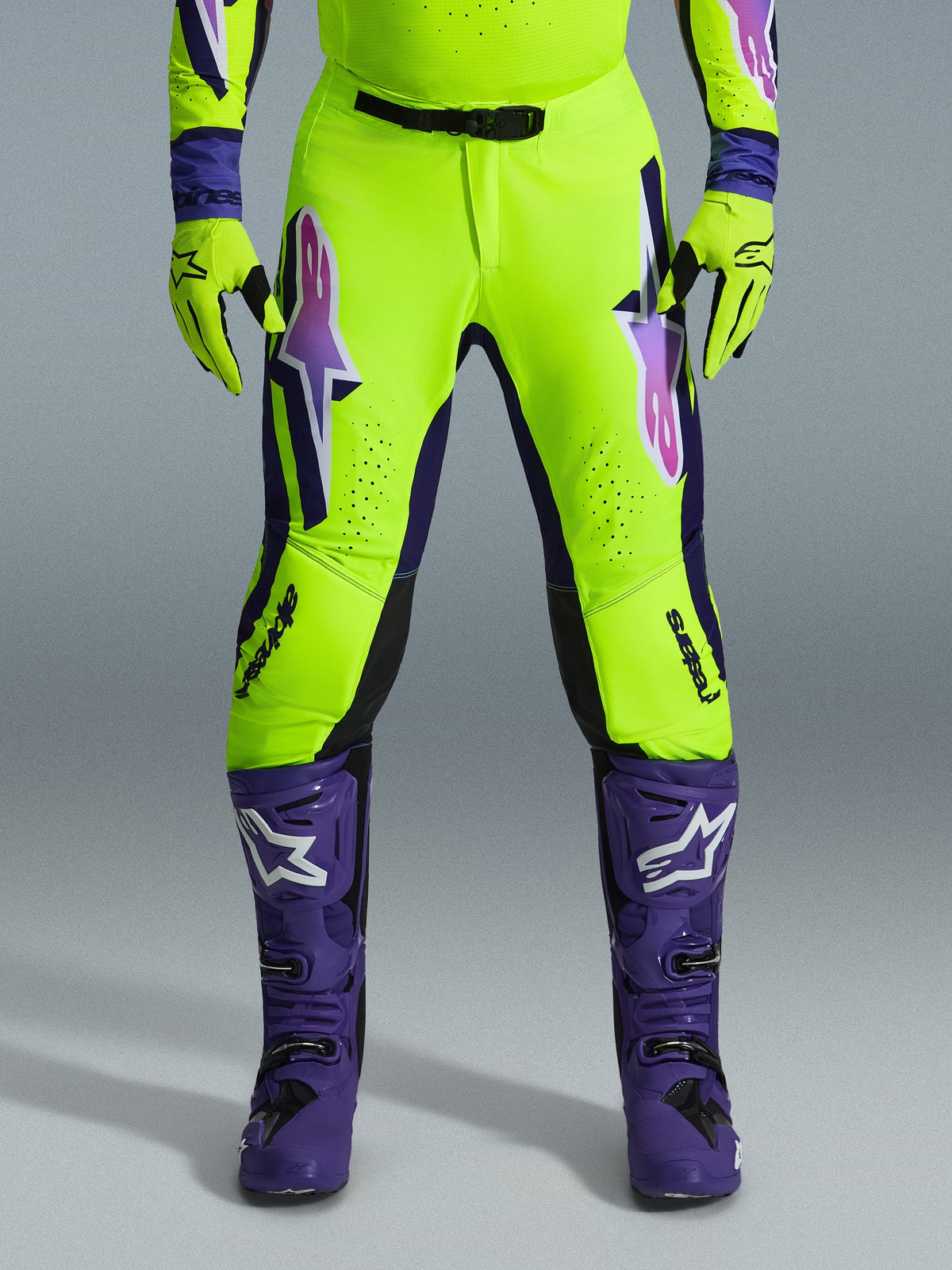 Alpinestars 2026 Supertech Vista byxor, motocrossbyxor, neon-gul, lila och svart, bärs med matchande handskar och lila stövlar, med stora tonade logotyper på låren, perforerade zoner för ventilation och en professionell atletisk design för terrängkörning