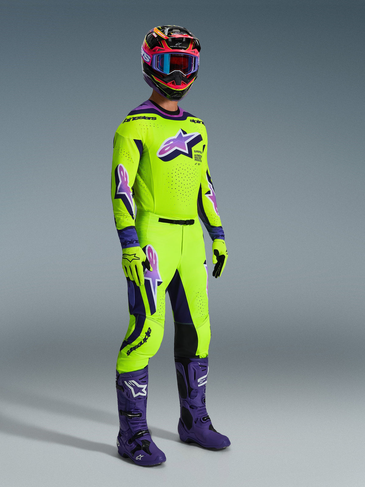 Alpinestars 2026 Supertech Vista-byxor, motocrossbyxor, neongula och lila, bärs med matchande racingtröja, lila stövlar och färgglad hjälm, med knäpaneler i svart läder, tydliga lila Astar-logotyper och perforerade ventilationszoner, koordinerad outfit för terrängkörning.
