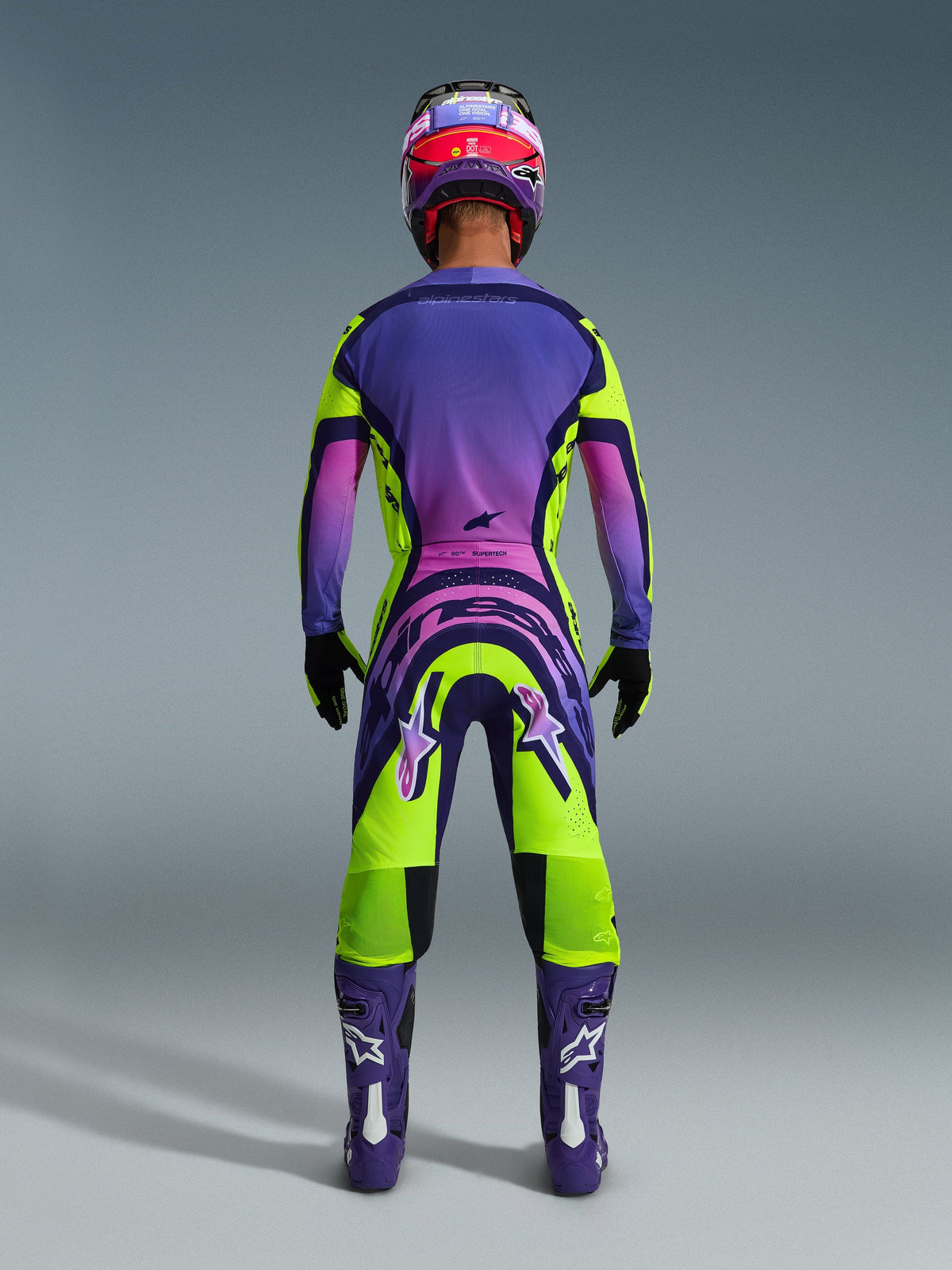 Alpinestars 2026 Supertech Vista byxor, motocrossbyxor, gul, lila och svart, baksida av en motocrossförare i en komplett racingutrustning med en lila gradient-tröja och lila stövlar, livfull atletisk design för professionell terrängkörning