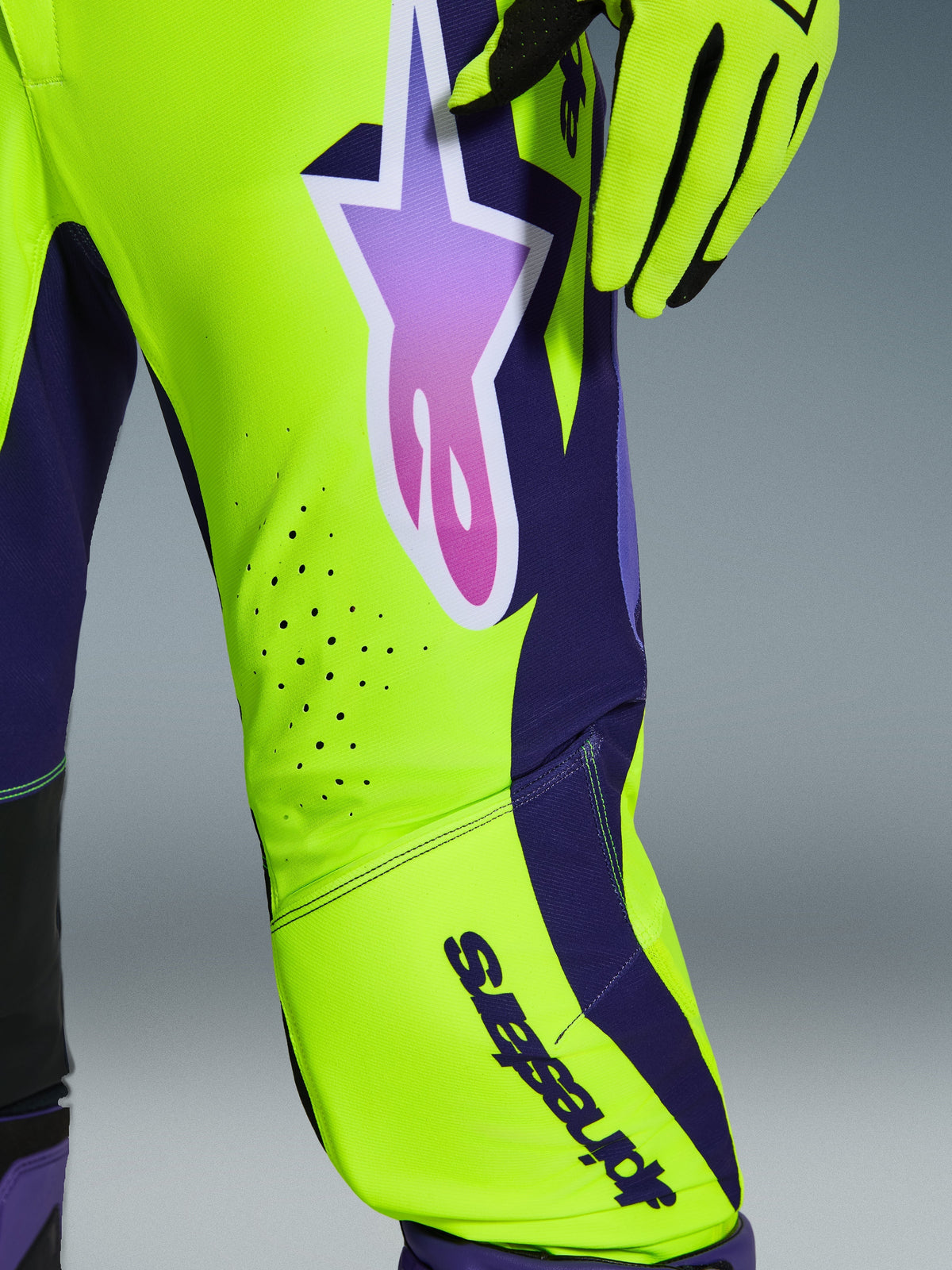 Alpinestars 2026 Supertech Vista-byxor, motocrossbyxor, gul, lila och svart, närbild som visar tonad stjärnlogotyp och laserskurna ventilationshål, tillsammans med matchande racinghandskar