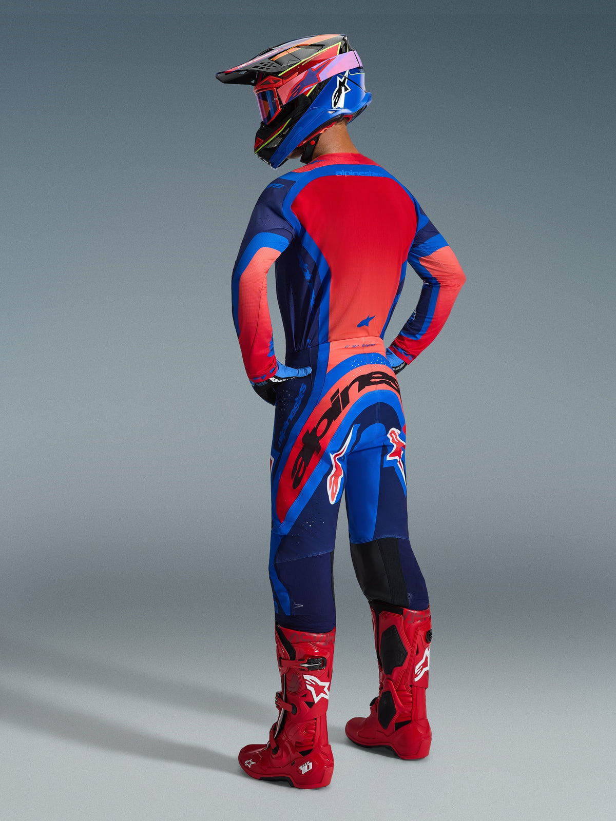 Alpinestars 2026 Supertech Vista Pants, Motocross Pants, Dark Navy Hot Coral and Cobalt, rear view on a rider wearing a matching racing jersey and red boots, featuring bold branding on the seat and durable stretch fabric for off-road performance.