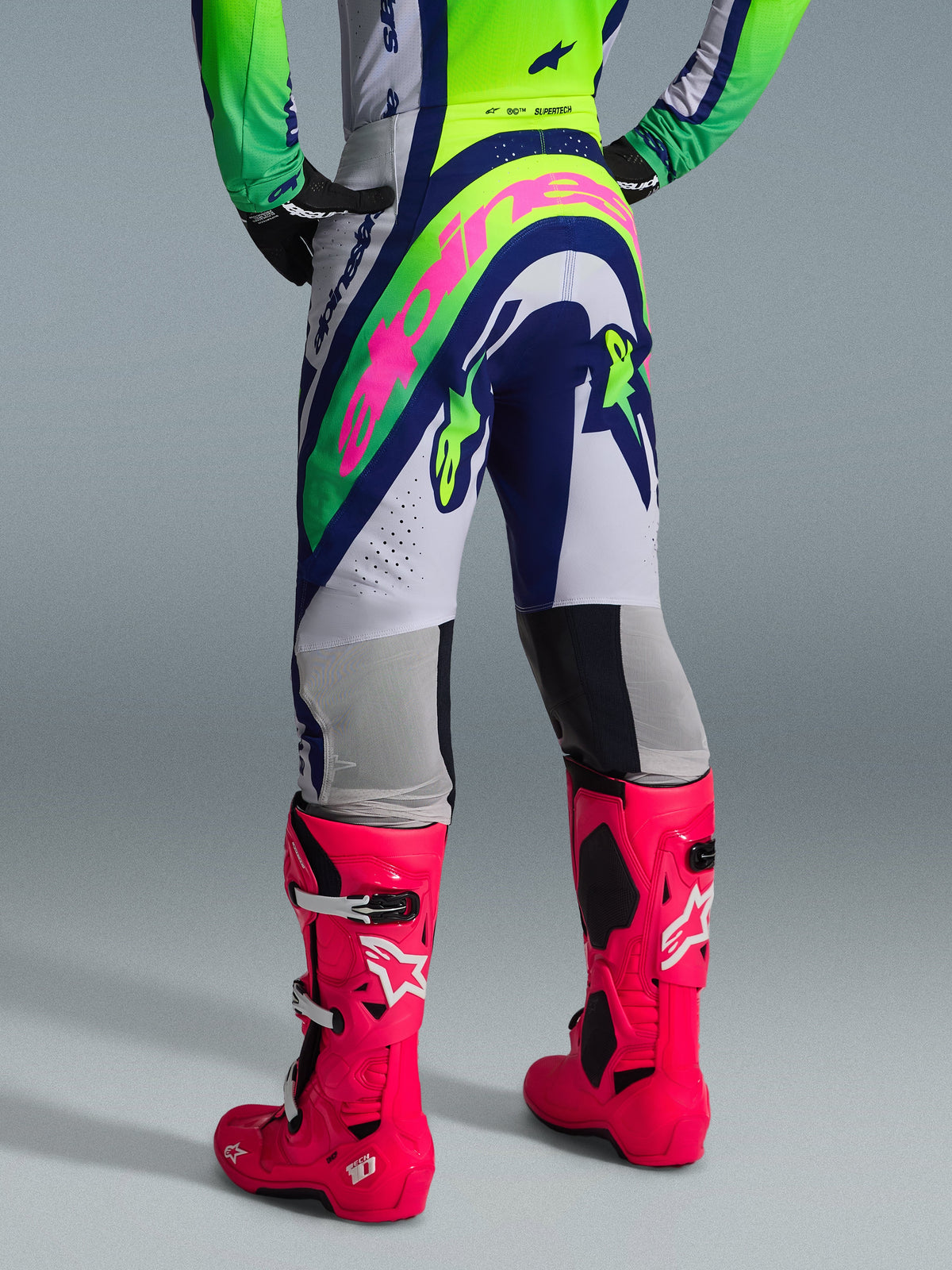 Alpinestars 2026 Supertech Vista Gear Set, rear view of motocross apparel, white pants with blue and lime green panels, large pink branding on seat, paired with vibrant pink Tech 10 boots, professional off-road racing gear