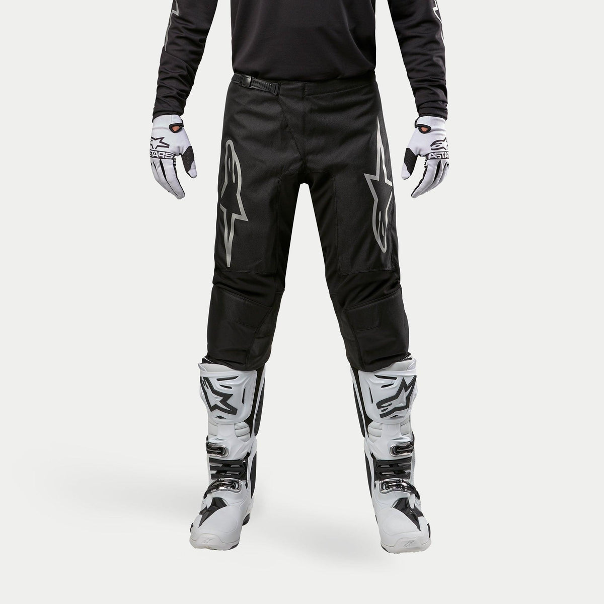 Alpinestars 2024 Fluid Graphite Pants, Motocross Pants, Black and Silver, featuring silver Alpinestars logos on the thighs, worn with white and black motocross boots and gloves, sporty design for off-road racing