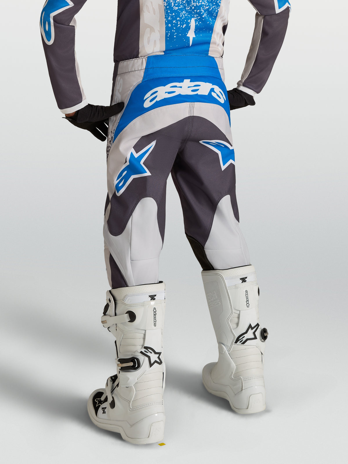 Alpinestars Youth Fluid Drag Pants in Graystone and UCLA Blue, motocross gear shown from behind on a rider with white boots.