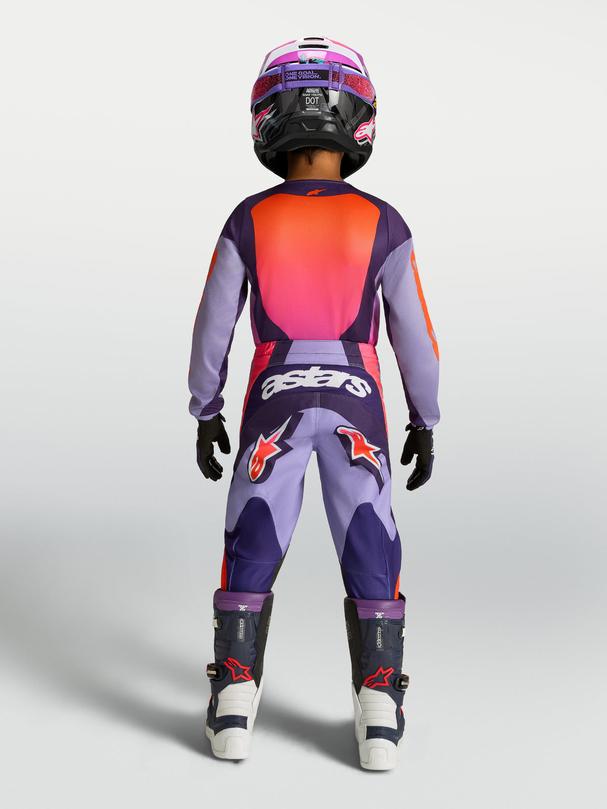 Alpinestars Ungdom Fluid Hunt byxor, motocrossbyxor i lila och rosa, slitstark 600D polytygskonstruktion, vy bakifrån på ung förare i full racingutrustning för terrängkörning.