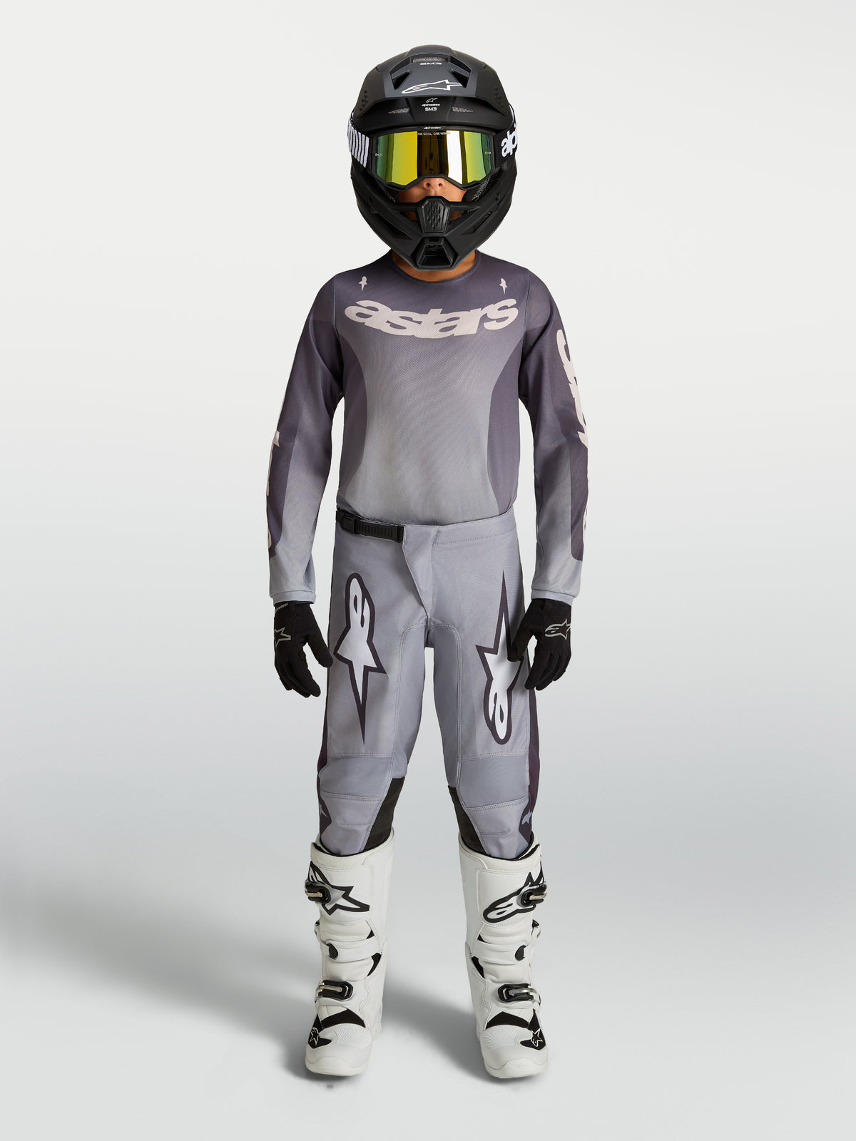 Alpinestars 2027 Fluid Amber ungdomsbyxor, grå och sandfärgade motocrossbyxor i 600D-polytyg, visas med matchande utrustning.