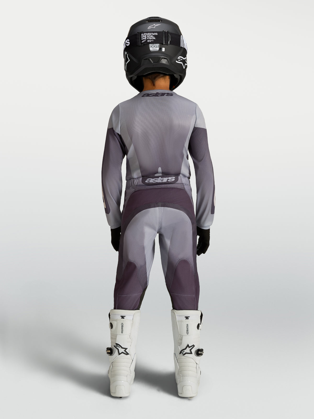 Alpinestars 2027 Fluid Amber ungdomsbyxor, motocrossbyxor för terrängkörning, sandfärgade och gråa, vy bakifrån på en förare, slitstarkt 600D-polytyg med stretchpaneler.