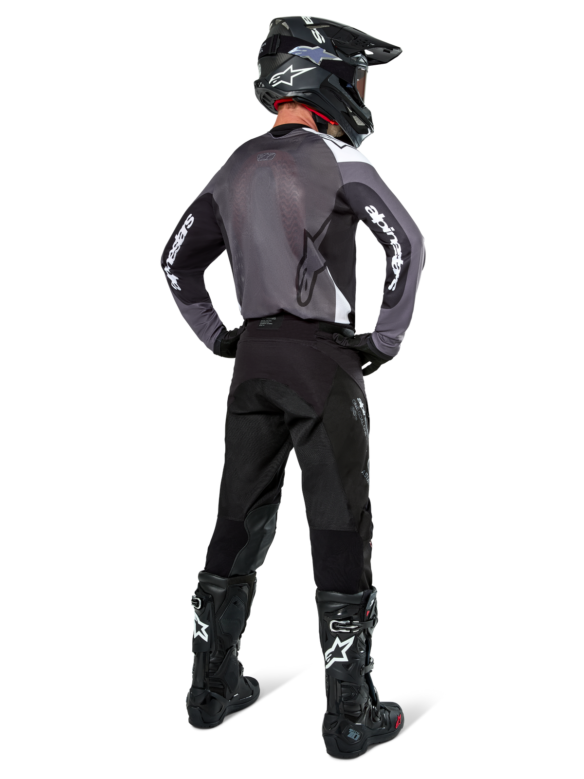 Motocrossförare iklädd Alpinestars Pro-Dura-tröja i Black Magnet White, vy bakifrån som visar grå ryggpanel i mesh och svarta ärmar med vit Alpinestars-logotyp, matchad med svarta byxor, svart hjälm och svartvita stövlar, professionell racingutrustning för enduro