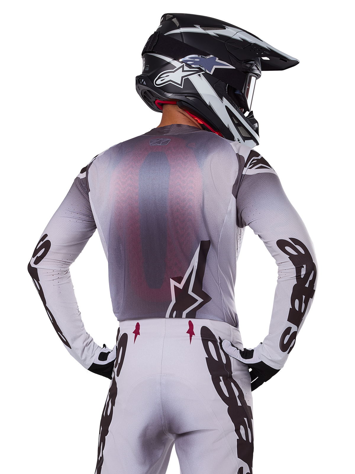 Motocrossförare sedd bakifrån iklädd Alpinestars 2025 Supertech Maker-tröja, silver och svart med röd ryggpanel i mesh och svarta logotyper på ärmarna, matchande motocrossbyxor och en svartvit hjälm, professionell racingutrustning för terrängkörning