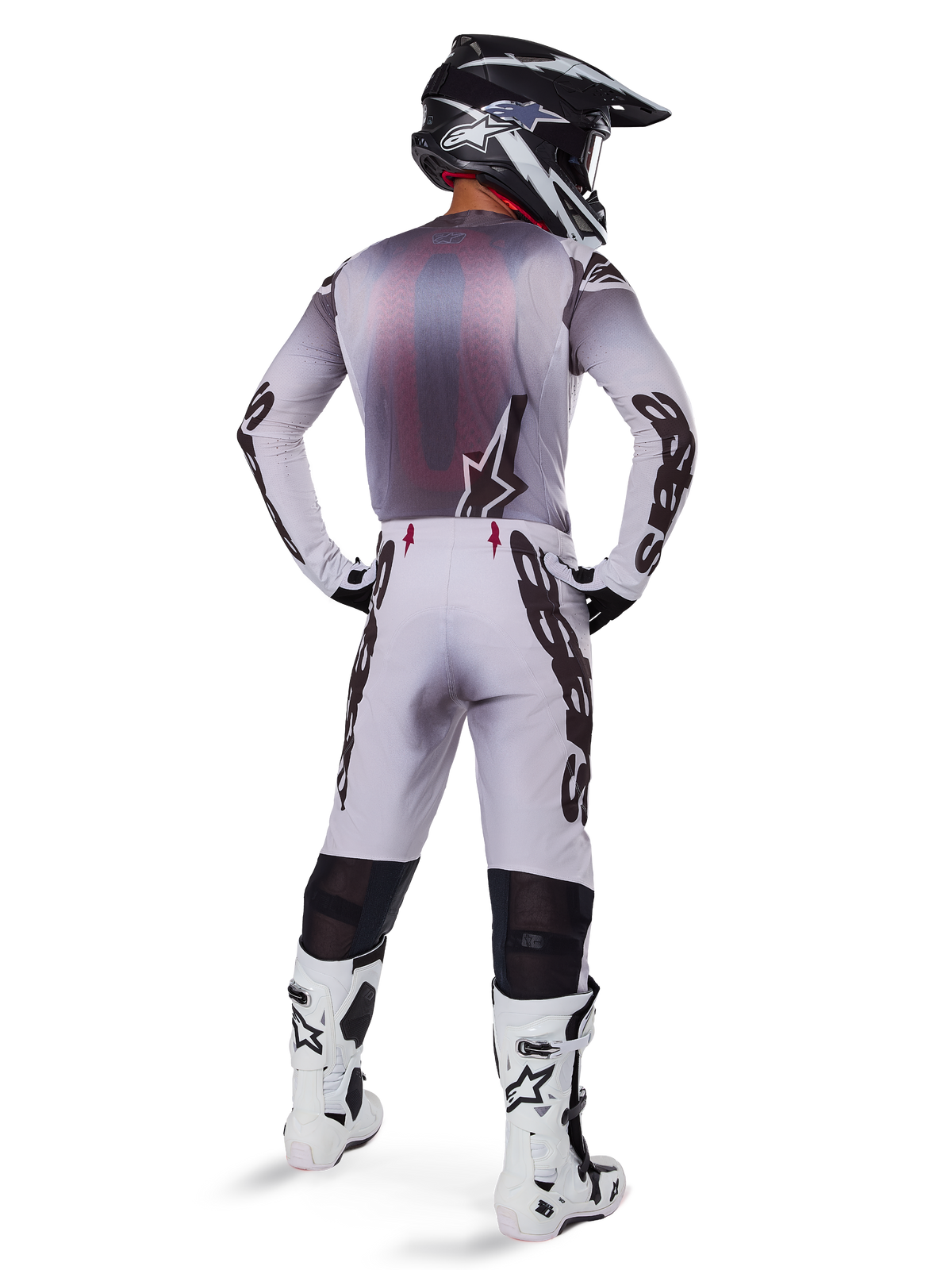 Motocrossförare sedd bakifrån iförd Alpinestars 2025 Supertech Maker-byxor i Silver och Svart, matchande långärmad tröja, svartvit hjälm och vita stövlar med svarta detaljer, framträdande svart logotyp på benen, professionell utrustning för terrängkörning