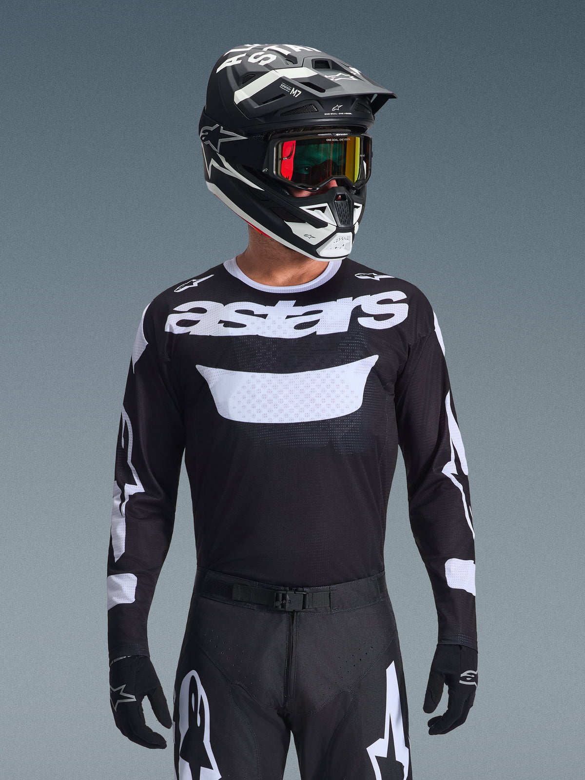 Motocross rider wearing the Alpinestars 2026 Racer Air Riway Gear Set, black jersey with white 'astars' logo and ventilated chest panel, black pants with white accents, matching black and white helmet with iridescent goggles, black gloves, high-performance motocross gear in black and white.