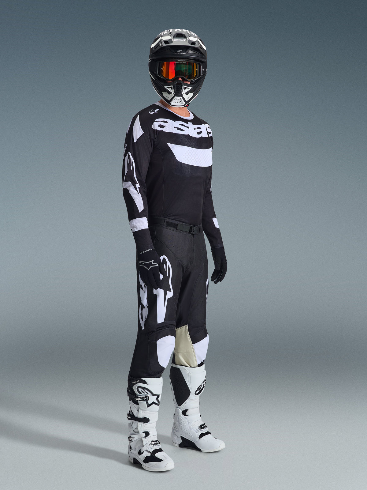 Alpinestars 2026 Racer Air Riway Gear Set, Motocross rider wearing complete racing gear, Black jersey with white 'Astars' branding and mesh panels, black pants with large white logos and knee panels, black helmet with red goggles, white and black boots, professional off-road racing outfit.