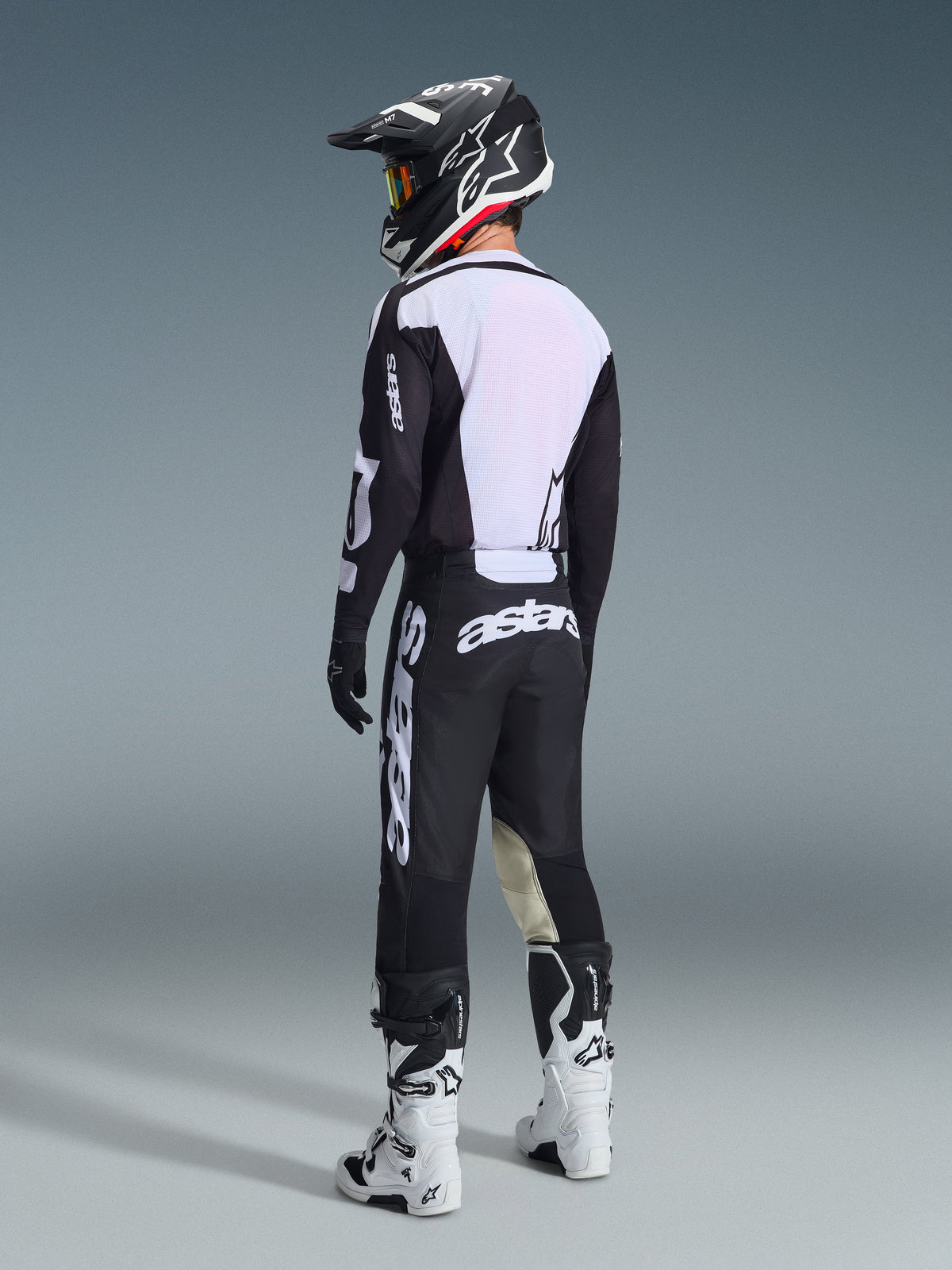 Motocross rider viewed from behind wearing the Alpinestars 2026 Racer Air Riway Gear Set in Black and White, featuring a ventilated mesh jersey back and large white branding, styled with a matching black helmet and white boots.