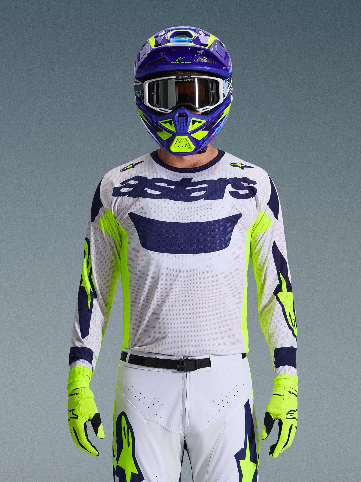 Motocrossförare som bär Alpinestars 2026 Racer Air Riway-utrustningsset, vit mesh-tröja med mörkblå 'astars'-logotyp och neongula detaljer, matchande vita byxor med mörkblå och neongul grafik, neongula handskar, lila och neongul hjälm med vita goggles, studiobild av en komplett racingutrustning för terrängkörning