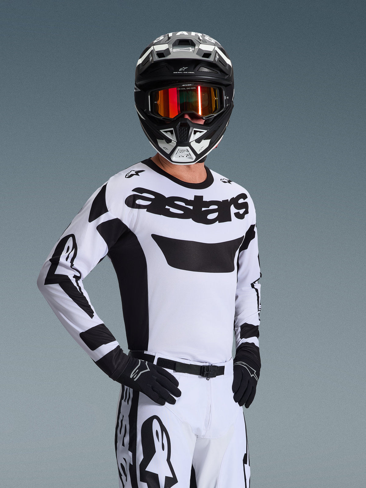 Alpinestars 2026 Racer Riway-tröja, motocrosströja, vit och svart, med framträdande 'astars'-logotyp på bröstet, bärs med matchande vita byxor och svarta handskar, svart och vit hjälm med röda reflekterande goggles, professionell offroad-racingutrustning