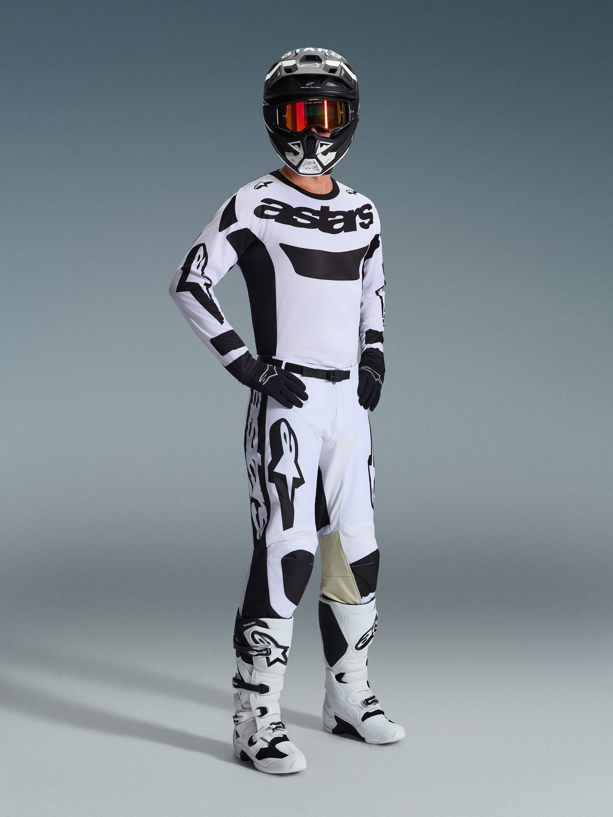 Motocrossförare i komplett racingutrustning, Alpinestars 2026 Racer Riway-tröja i vitt och svart, matchande vita och svarta motocrossbyxor, svart hjälm med spegelglasade goggles, vita och svarta stövlar och svarta handskar, koordinerad outfit för terrängkörning