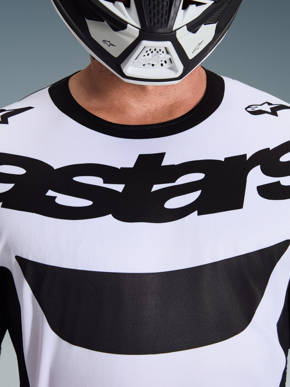 Närbild av en förare som bär Alpinestars 2026 Racer Riway-tröja i vitt och svart, med en tydlig 'astars'-logotyp över bröstet och en svart rundhalsad krage, kombinerat med en matchande motocrosshjälm.