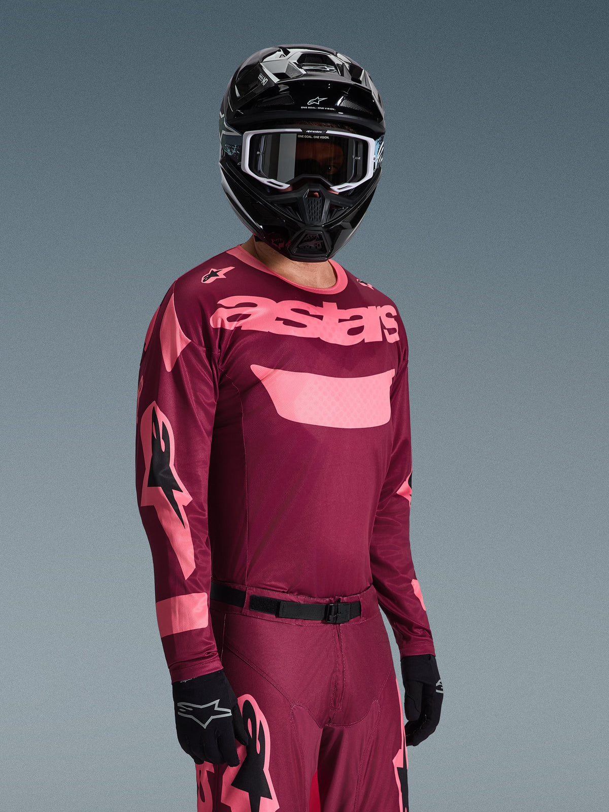 Motocrossförare i Alpinestars 2026 Racer Riway Gear Set, vinröd och rosa tröja med framträdande 'astars'-logotyp, matchande byxor med rosa detaljer, svart hjälm och handskar, professionell racingutrustning för terrängkörning
