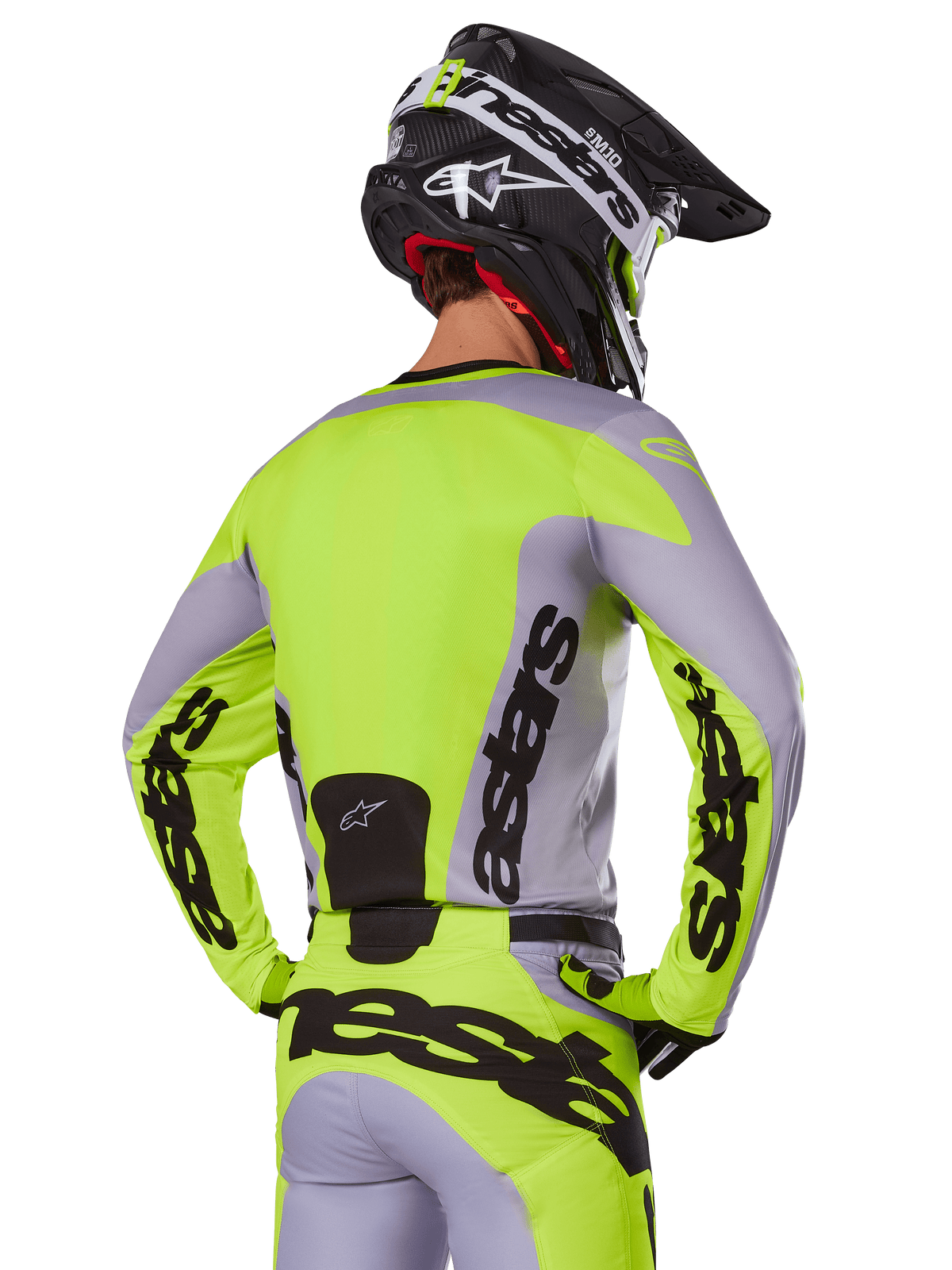 Motocross rider from behind wearing the Alpinestars 2025 Racer Veil Jersey in Gray and Yellow Fluo, featuring prominent 'astars' branding on the back and sleeves, paired with matching pants and a black helmet for a complete racing look.