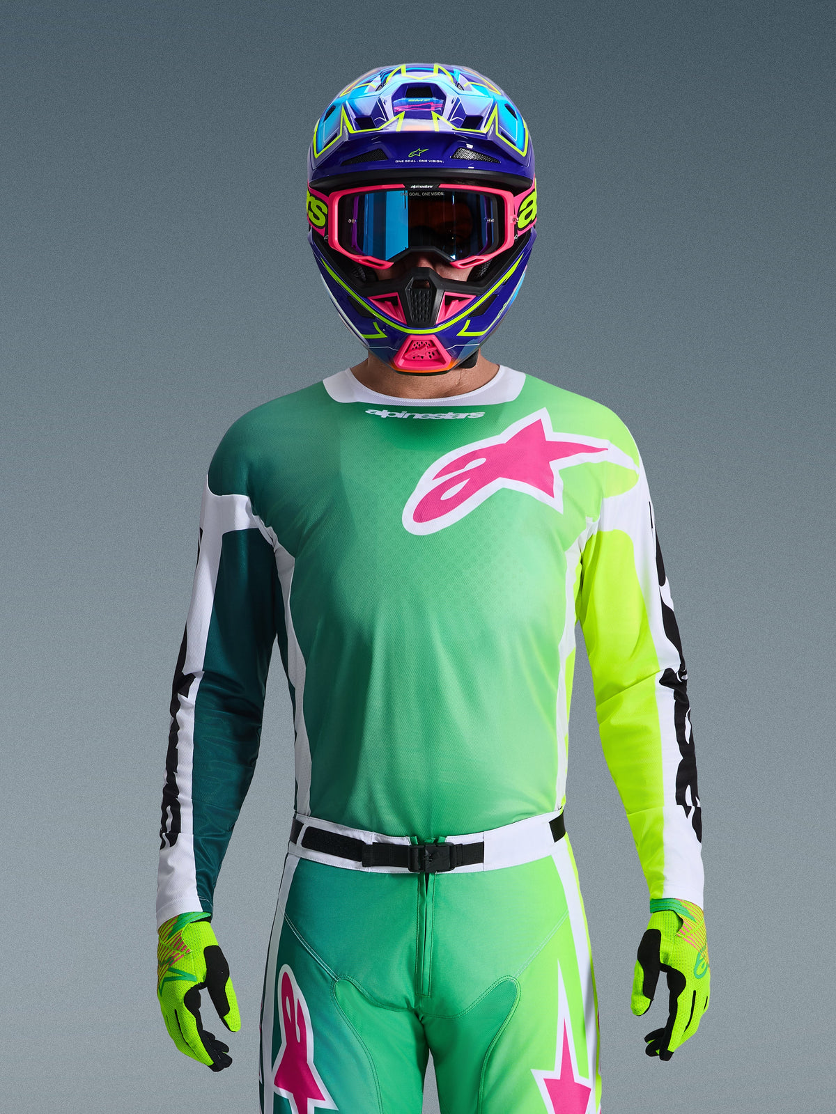 Alpinestars 2026 Racer Portl Gear Set, Motocross Rider wearing Green and Yellow gradient jersey with Pink Astars logo, matching pants, colorful blue and pink helmet with blue goggles, and lime green gloves, coordinated professional off-road racing outfit