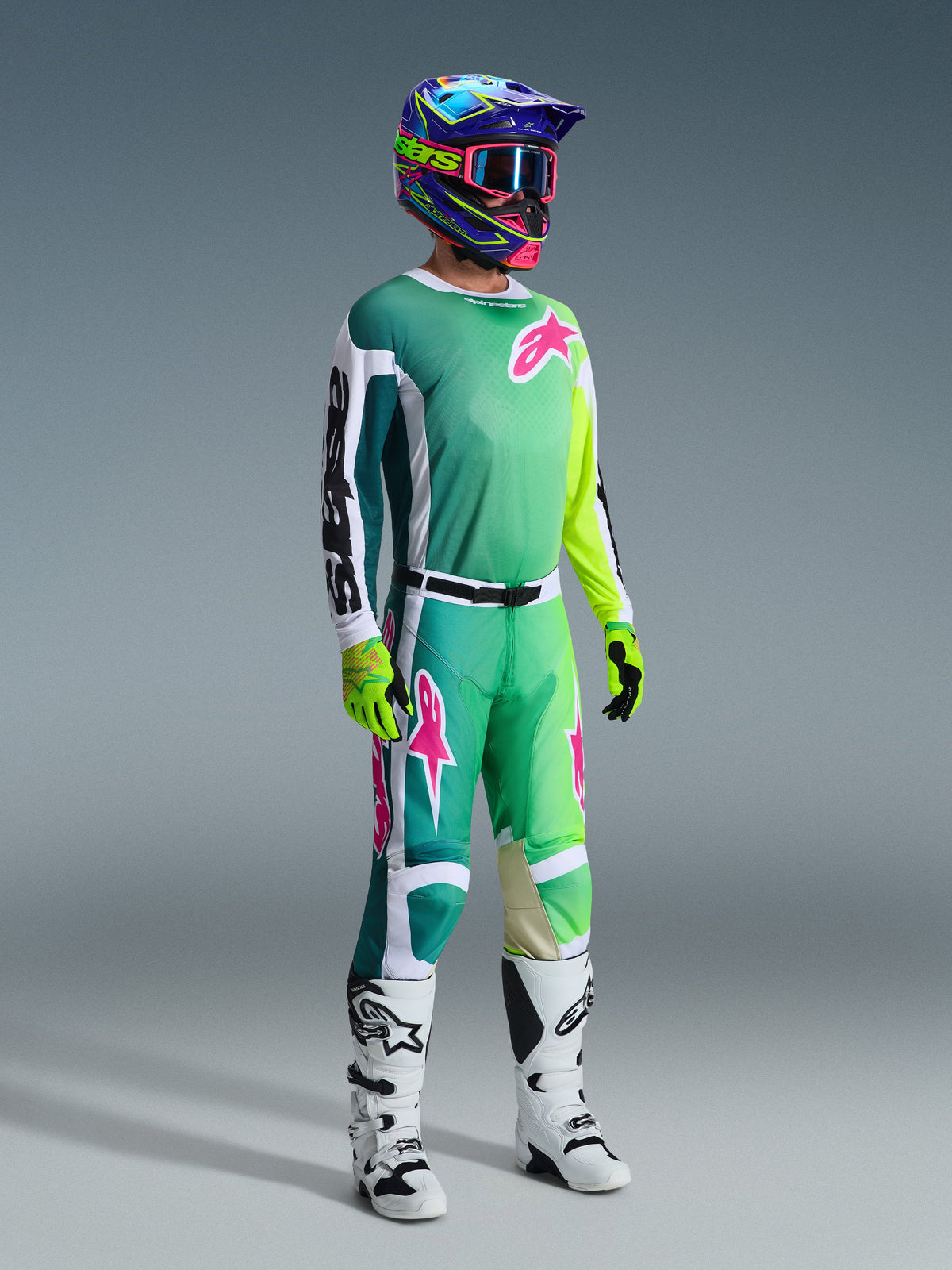Alpinestars 2026 Racer Portl Gear Set, Motocross rider in teal to lime green gradient jersey with pink logos and white sleeves, matching green and white pants, colorful graphic helmet with pink goggles, white boots, and fluorescent yellow gloves, professional off-road racing kit.