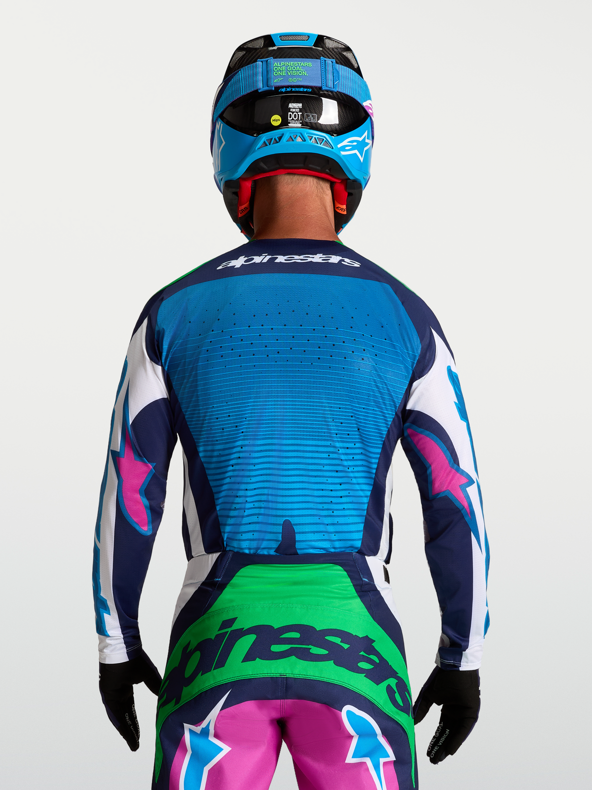 Alpinestars Techstar Maven tröja för terrängkörning, blå och grön med rosa detaljer, bärs av en modell bakifrån med hjälm och handskar, laserskuren ventilation för optimalt luftflöde.