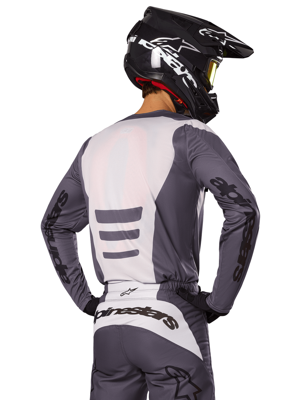 Motocrossförare sedd bakifrån iförd Alpinestars 2025 Fluid Haul-utrustningsset, grå och vit tröja och byxor, svart hjälm med vit grafik, gula goggles, matchande motocross-racingoutfit
