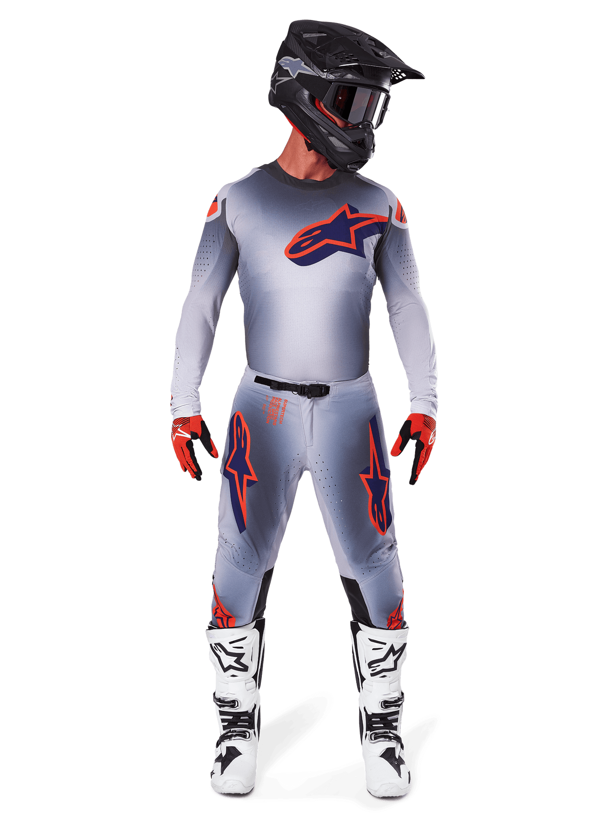 Motocrossförare iförd 2025 Supertech Lipan utrustningsset i Gray Orange Fluo, grå tröja med orangea detaljer och marinblå Alpinestars-logotyp, matchande grå byxor med stora logotyper på låren, matt svart hjälm, vita och svarta stövlar samt röda och svarta handskar, komplett racingoutfit på proffsnivå